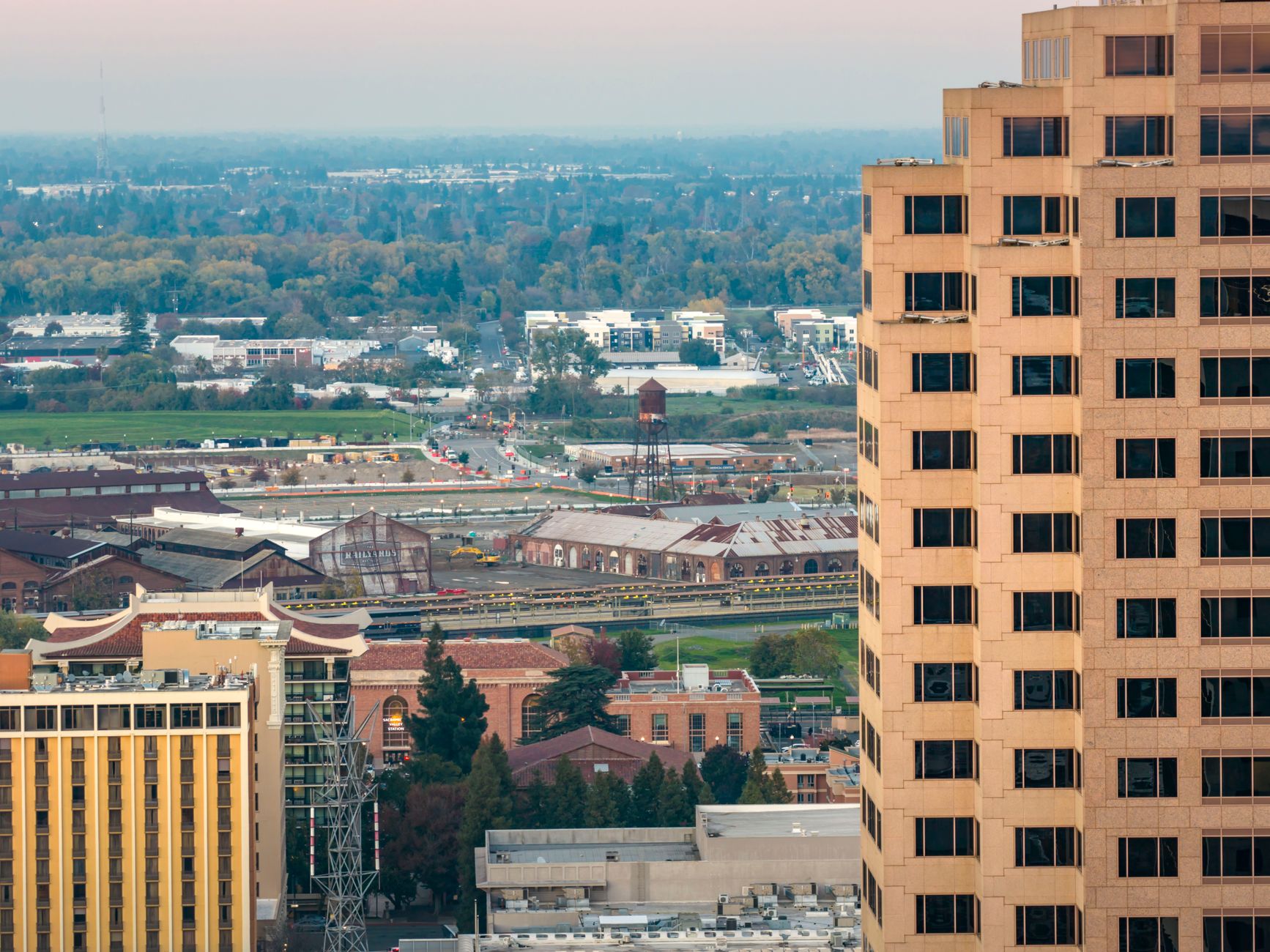 Detailed aerial view of Sacramento's urban landscape featuring diverse architecture and distant greenery in daylight.