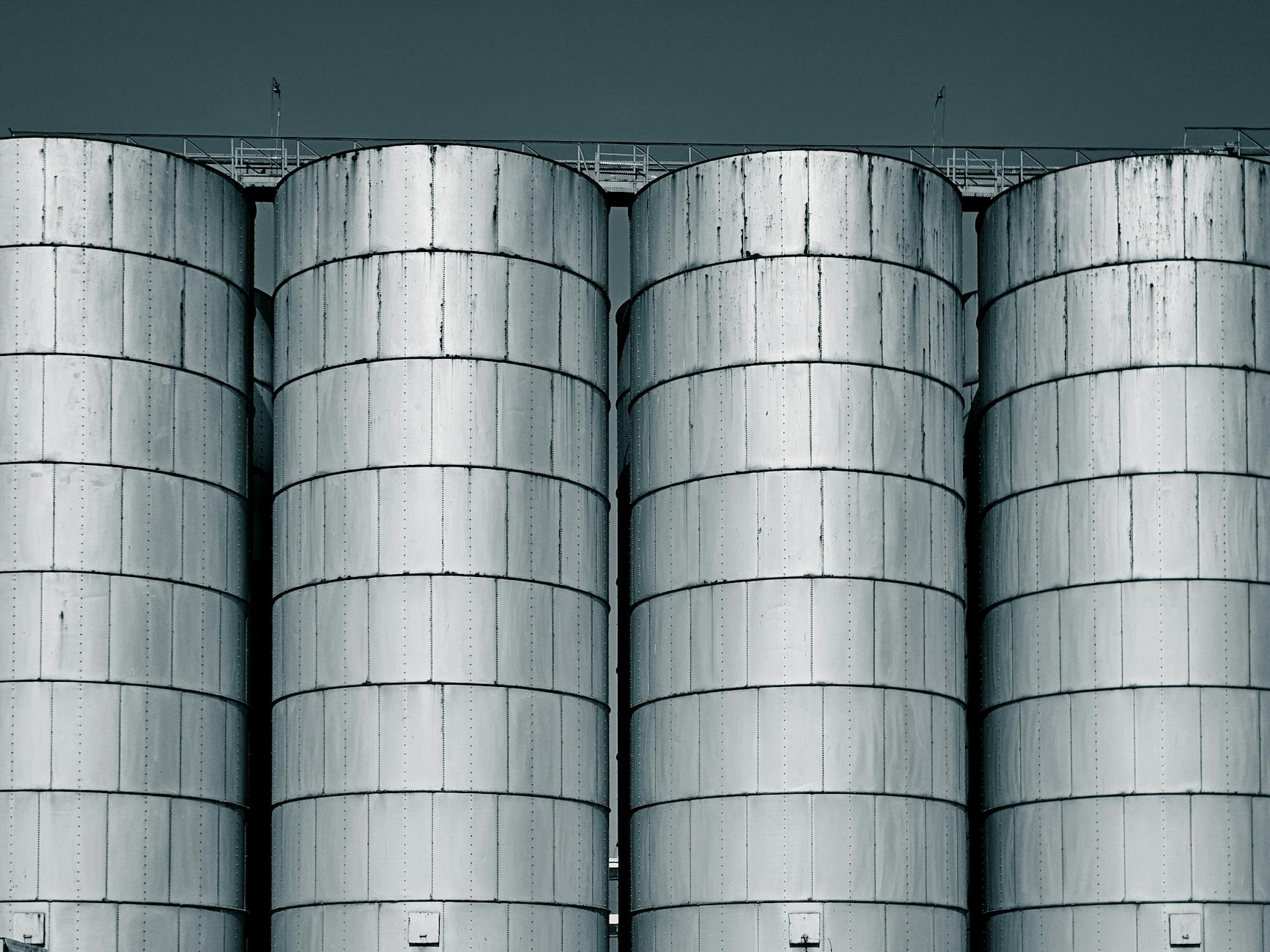 Four large industrial steel silos with a cool-toned sky backdrop.