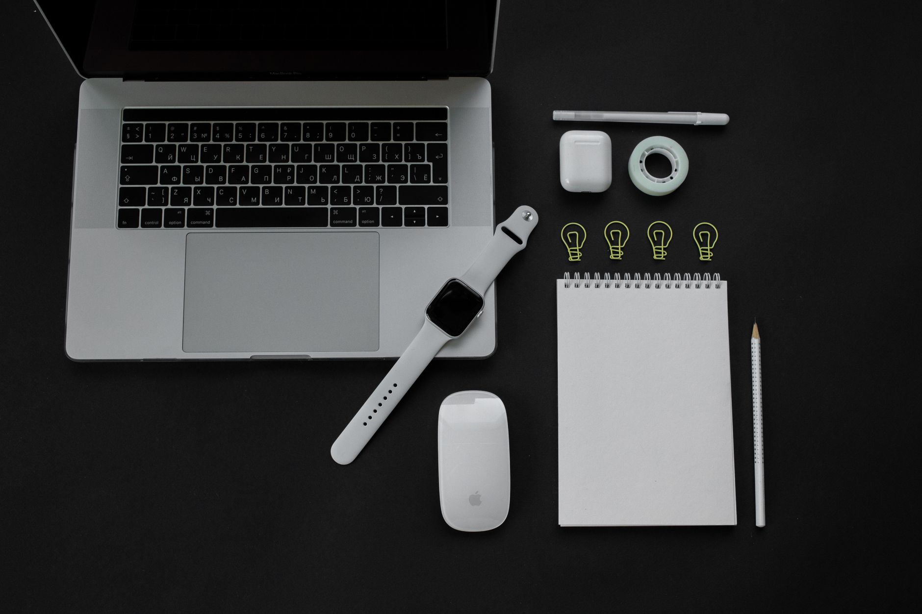 Flatlay of modern gadgets including laptop, smartwatch, and accessories on black surface.