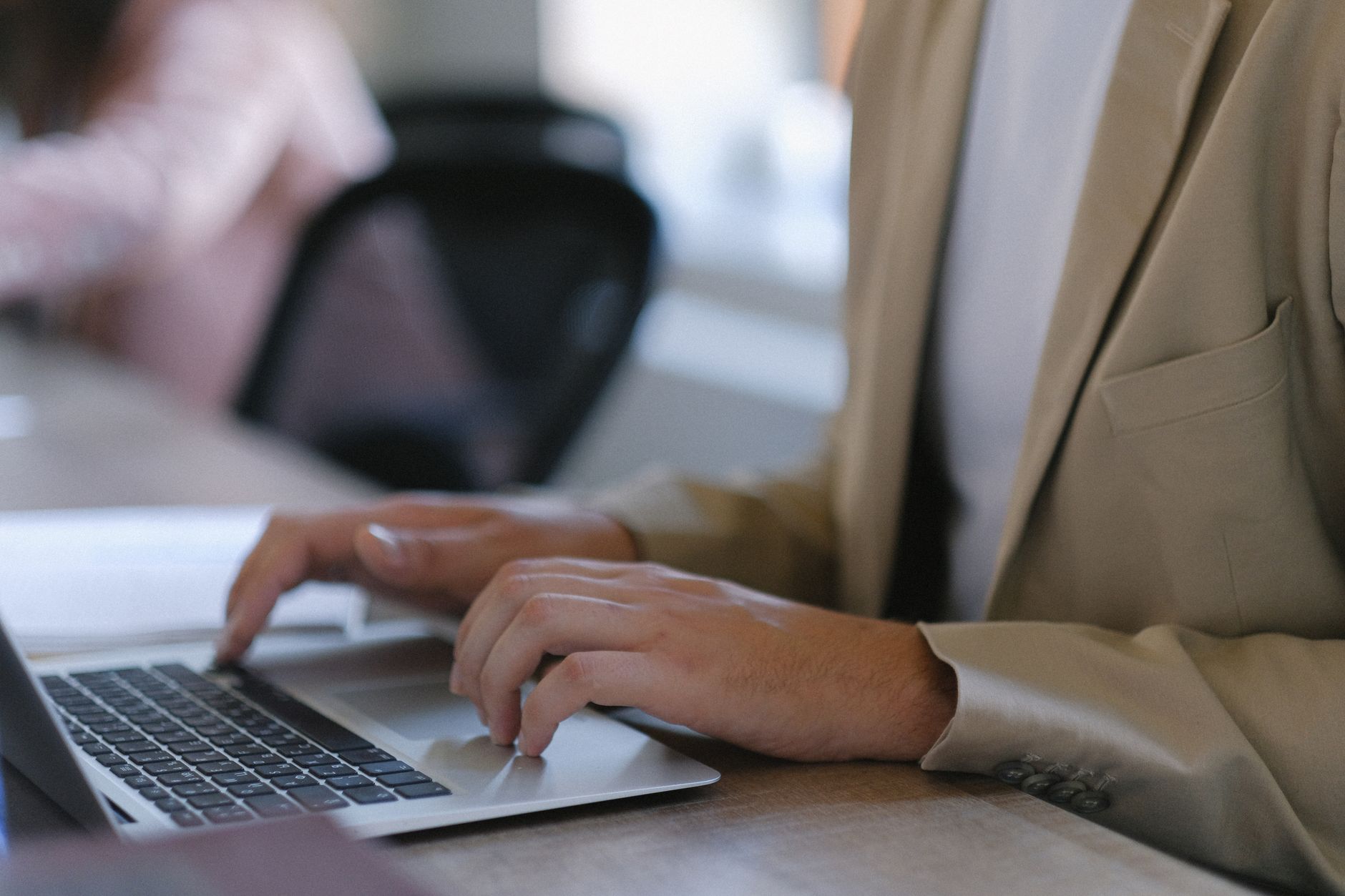 Unrecognizable male worker in formal wear browsing modern netbook while sitting at table during work in office with colleague on blurred background