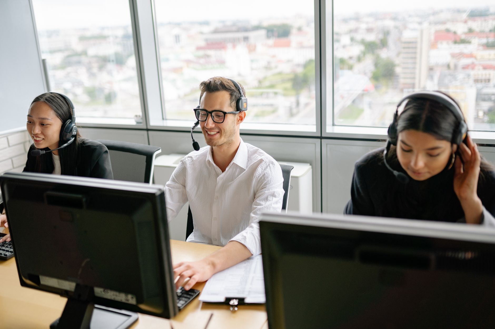 Group of call center employees wearing headsets, collaborating in a bright office environment.
