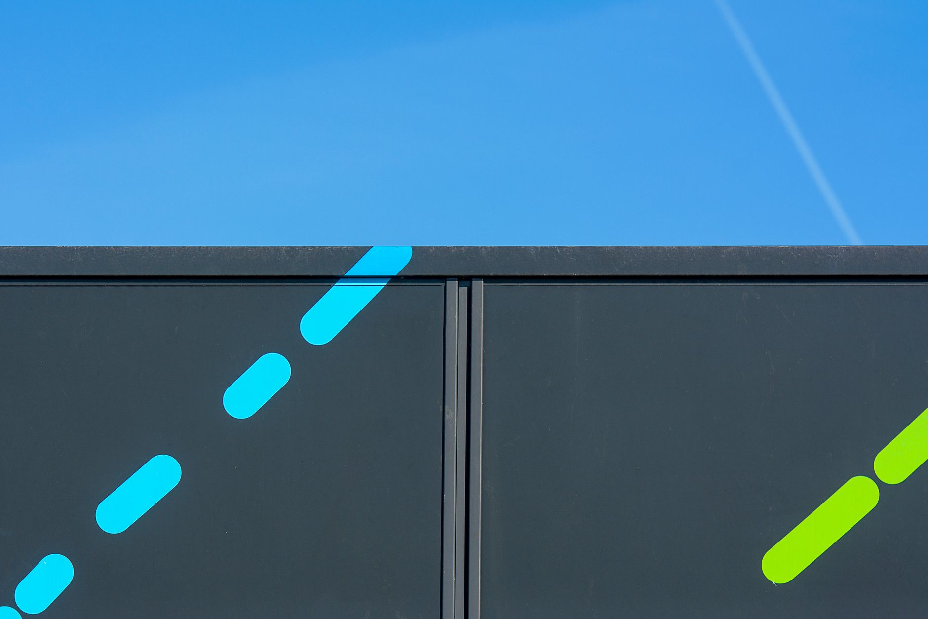 A minimalist view of a dark metal gate with colorful stripes against a vibrant blue sky.