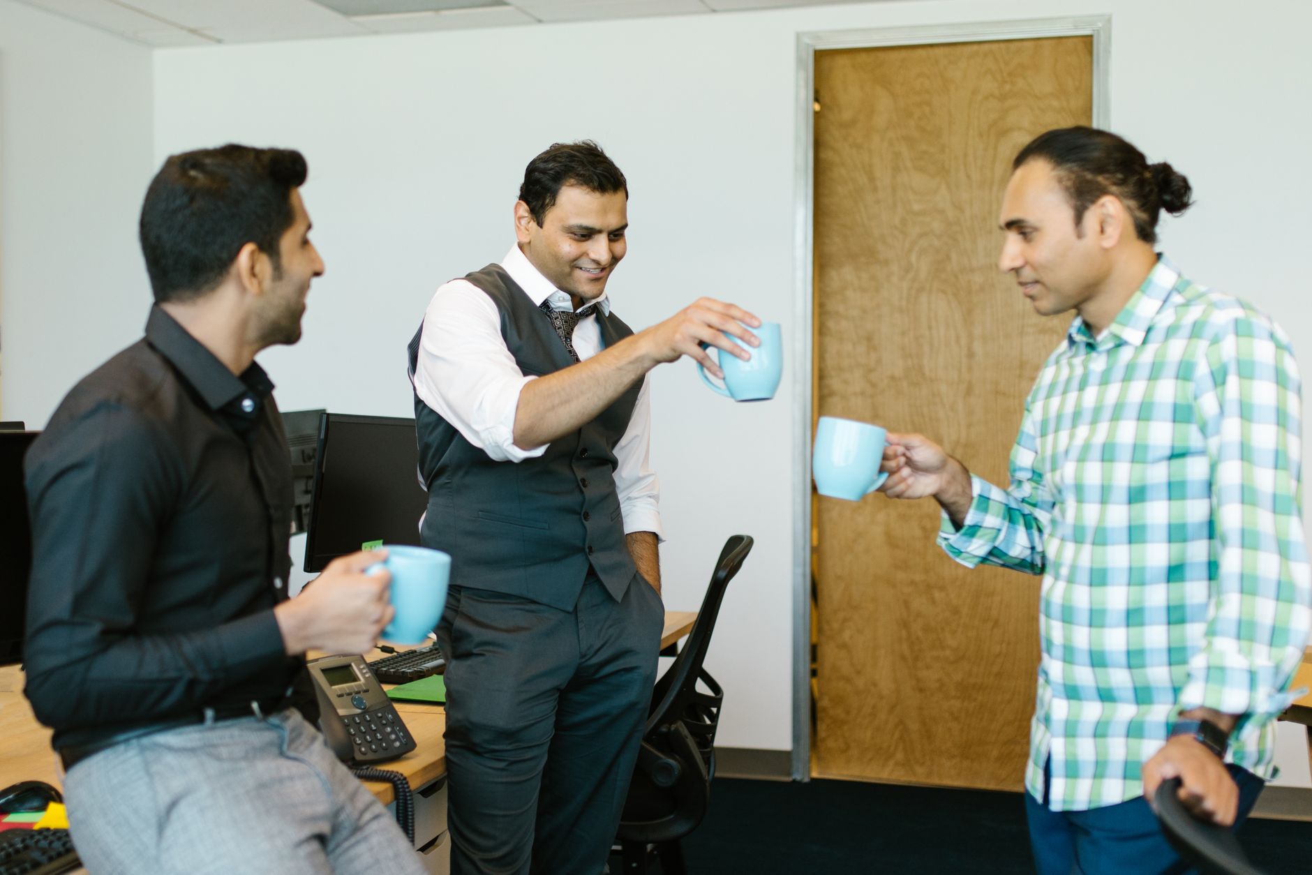 Three colleagues enjoying a coffee break, sharing smiles and conversations in a modern office setting.