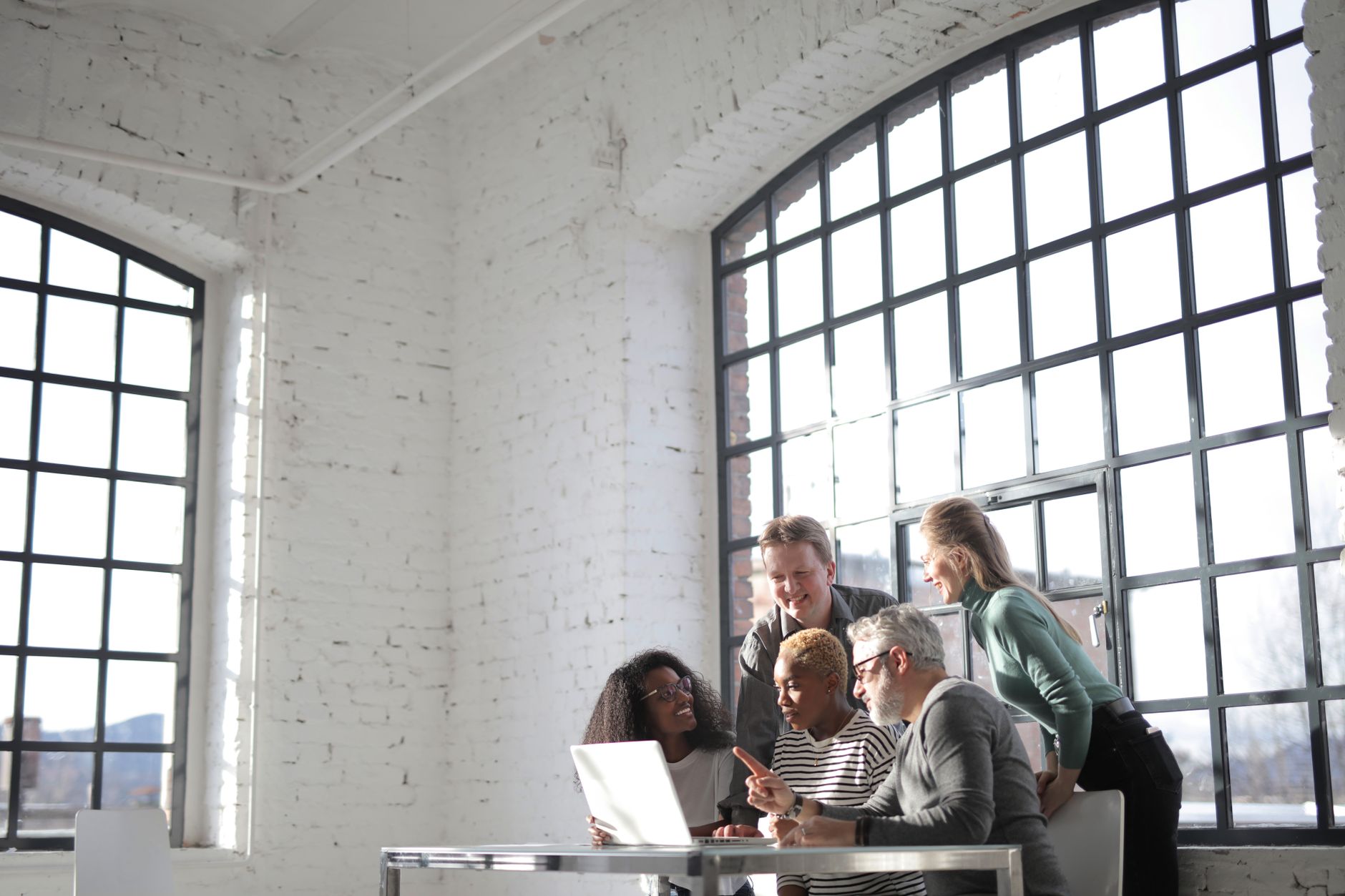 Group of diverse colleagues of different ages discussing business ideas while working on laptop in creative workplace and looking at screen during work