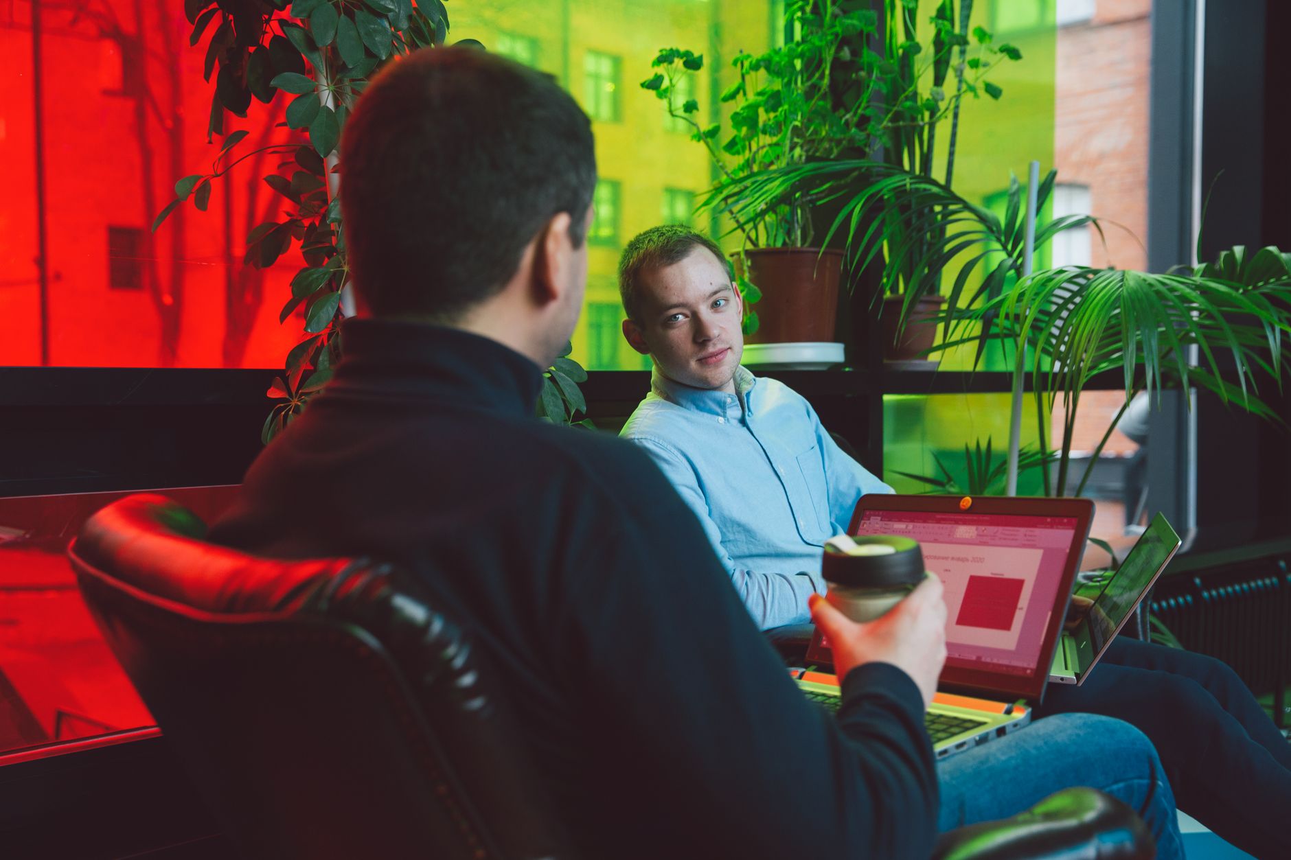 Two men having a casual work meeting with laptops and coffee in a modern indoor setting.