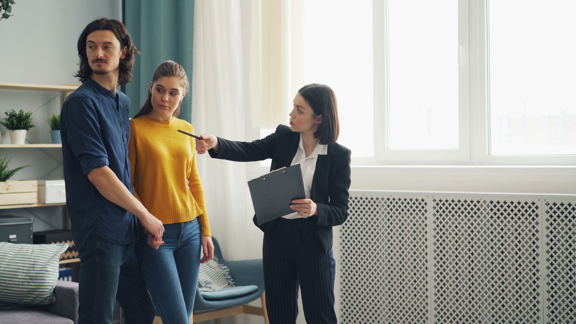 A real estate agent showing a house to a young couple, discussing details in a brightly lit room.