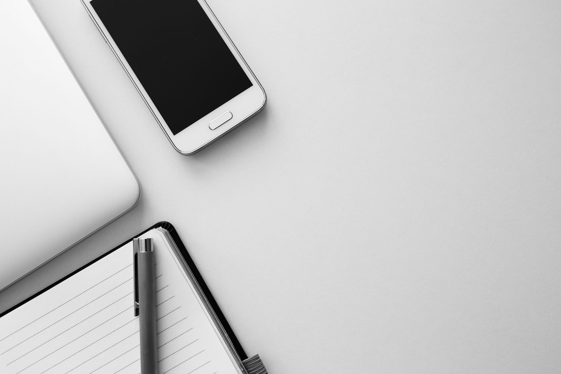 Flat lay of a modern workspace with smartphone, notebook, and pen on a neutral background.