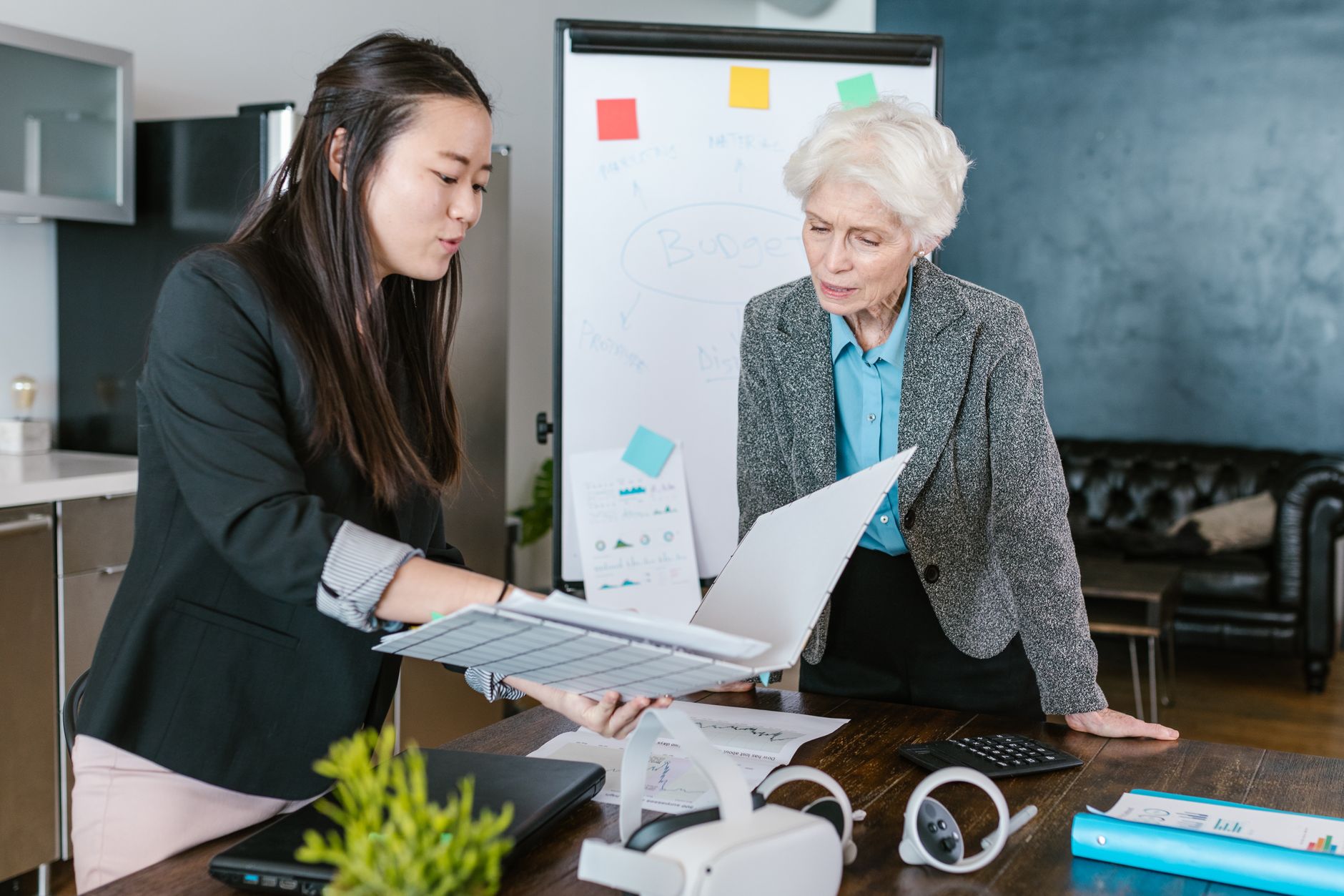 An Asian and a senior Caucasian woman engaged in a business discussion in an office setting.