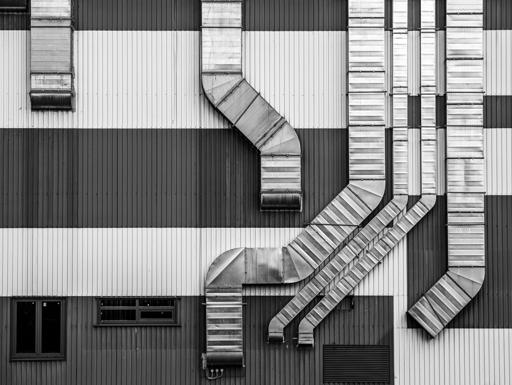 Monochrome image showcasing industrial ductwork and vents on a striped building exterior.