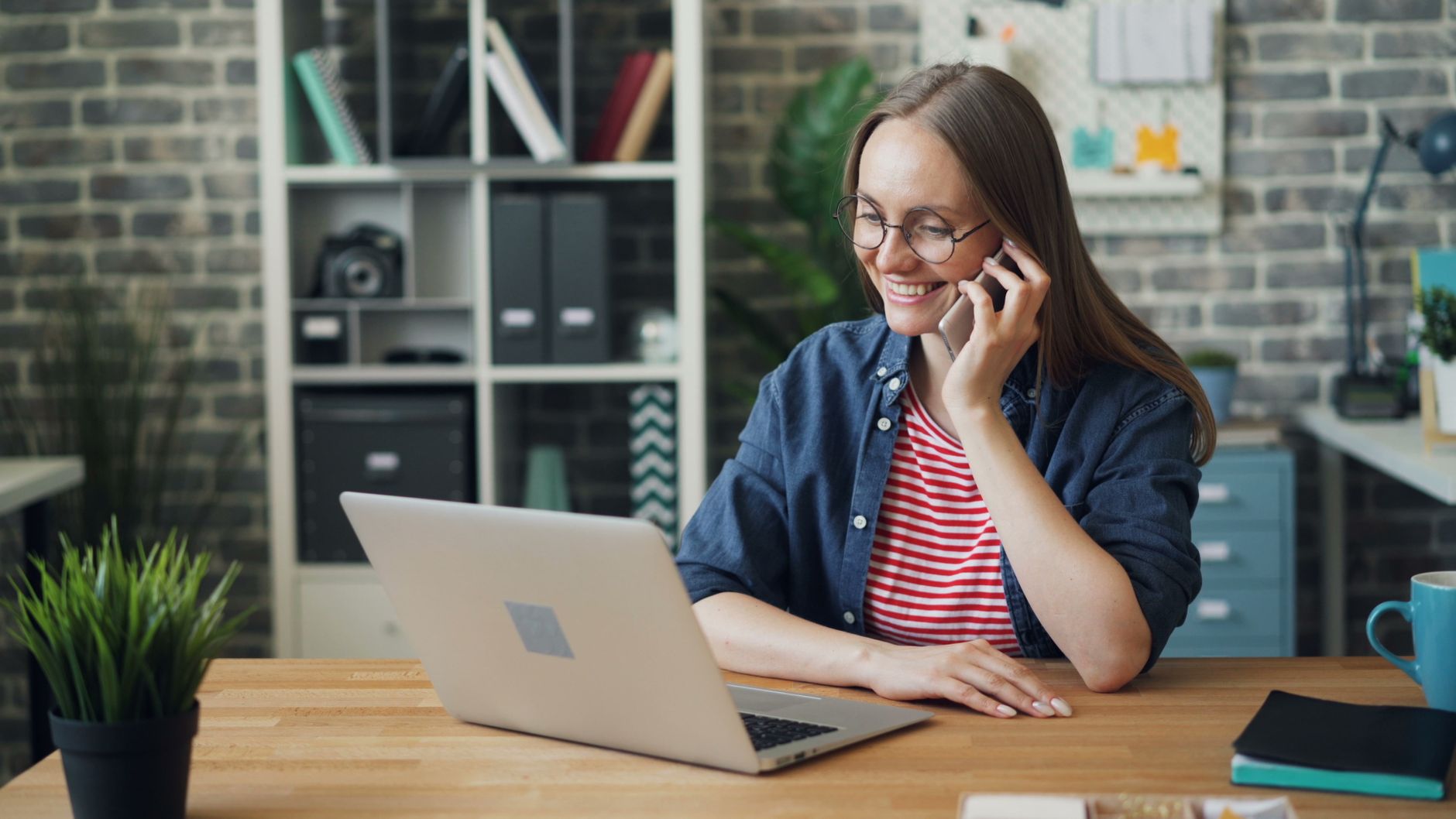 Young woman in a modern office using a smartphone and laptop, smiling and working efficiently.