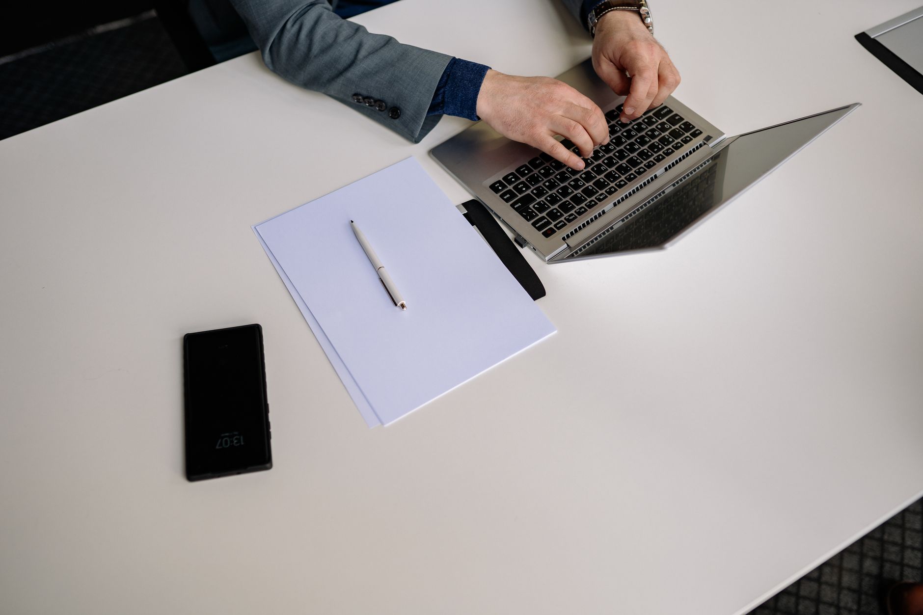 Top view of businessman typing on a laptop at a neat white desk with phone and papers.