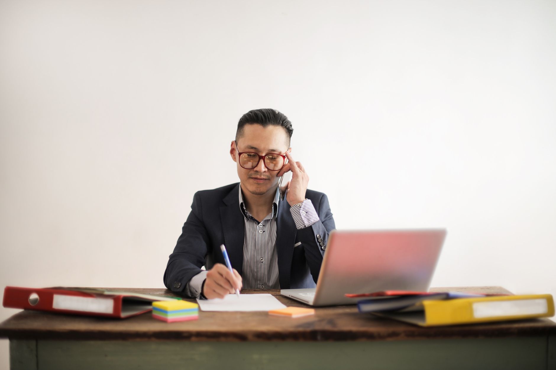 Focused businessman multitasking at desk, engaged in a phone call and working on a laptop.