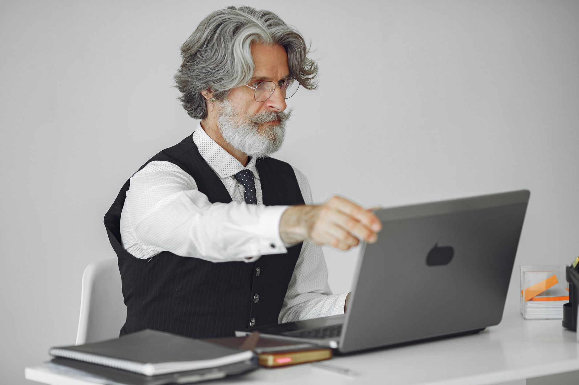 Senior man with gray hair working on a laptop in an elegant office setting, wearing a suit.