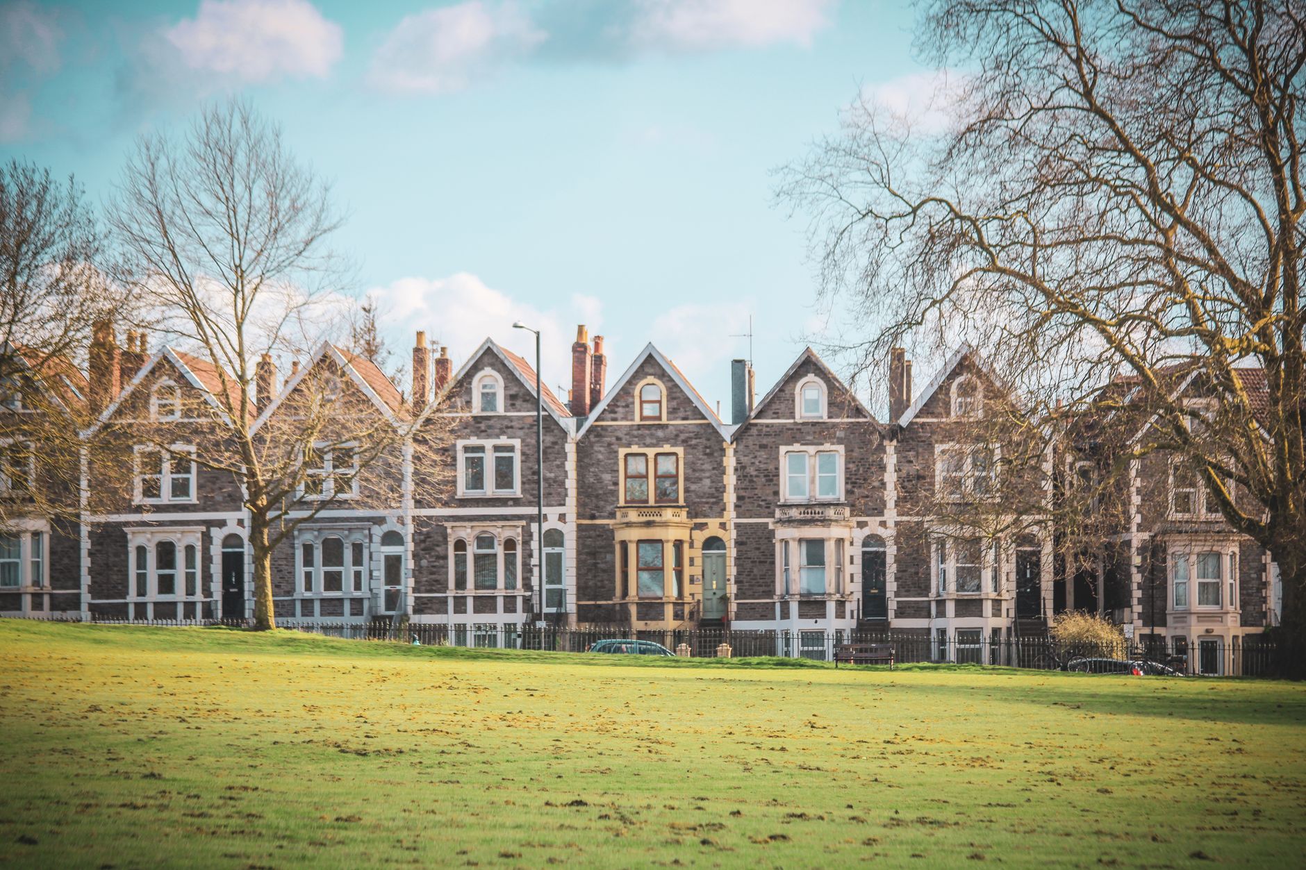 Victorian terraced houses in Bristol, England, set against a lush green park with clear skies.
