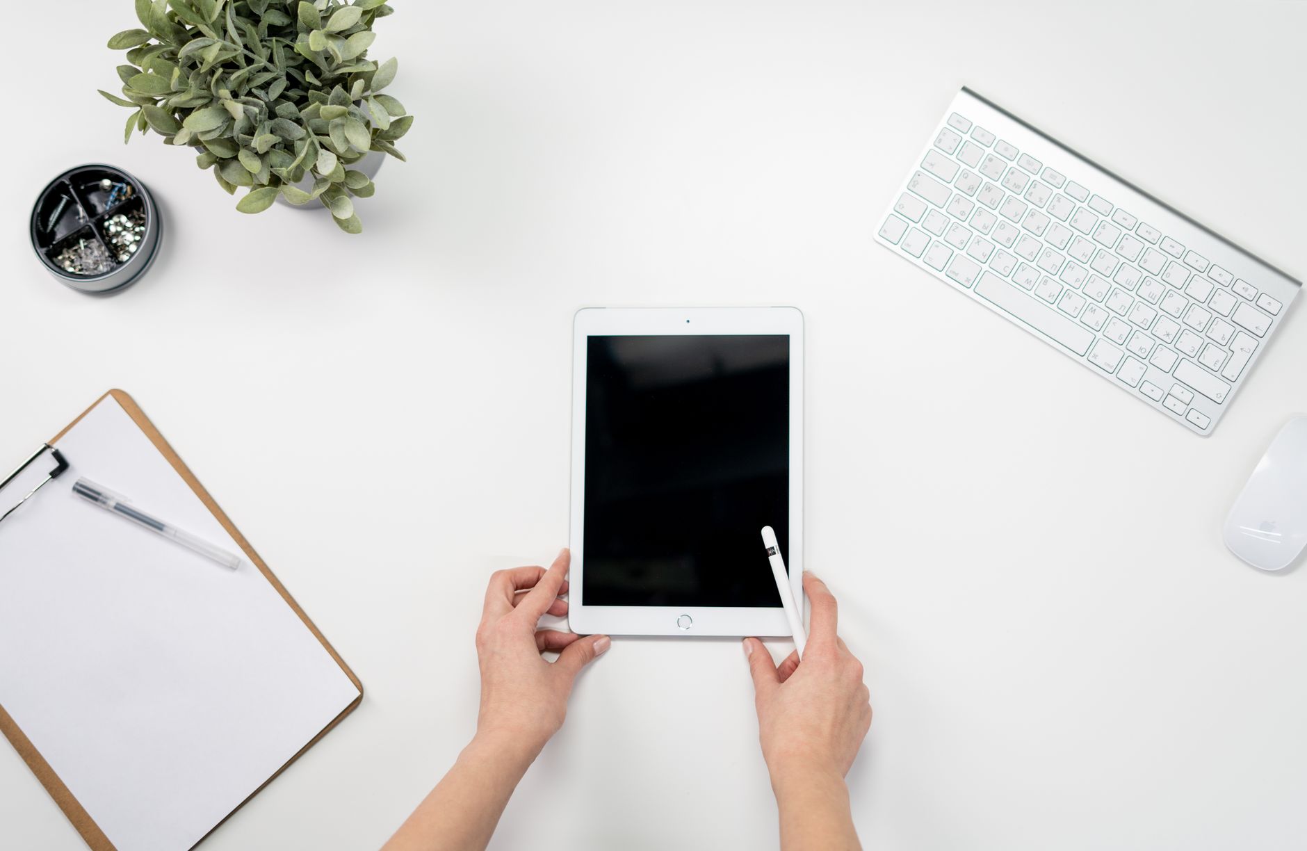 A clean workspace with a tablet, keyboard, mouse, and stationery on a white table.