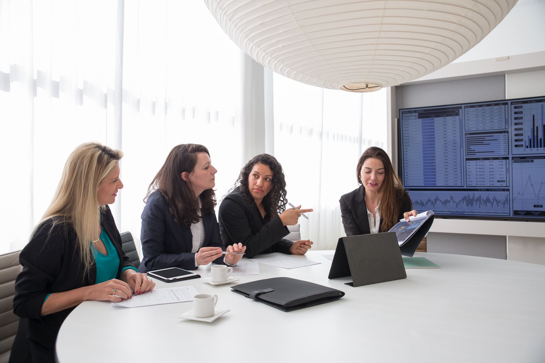Businesswomen discussing reports during a meeting in a contemporary office setting.