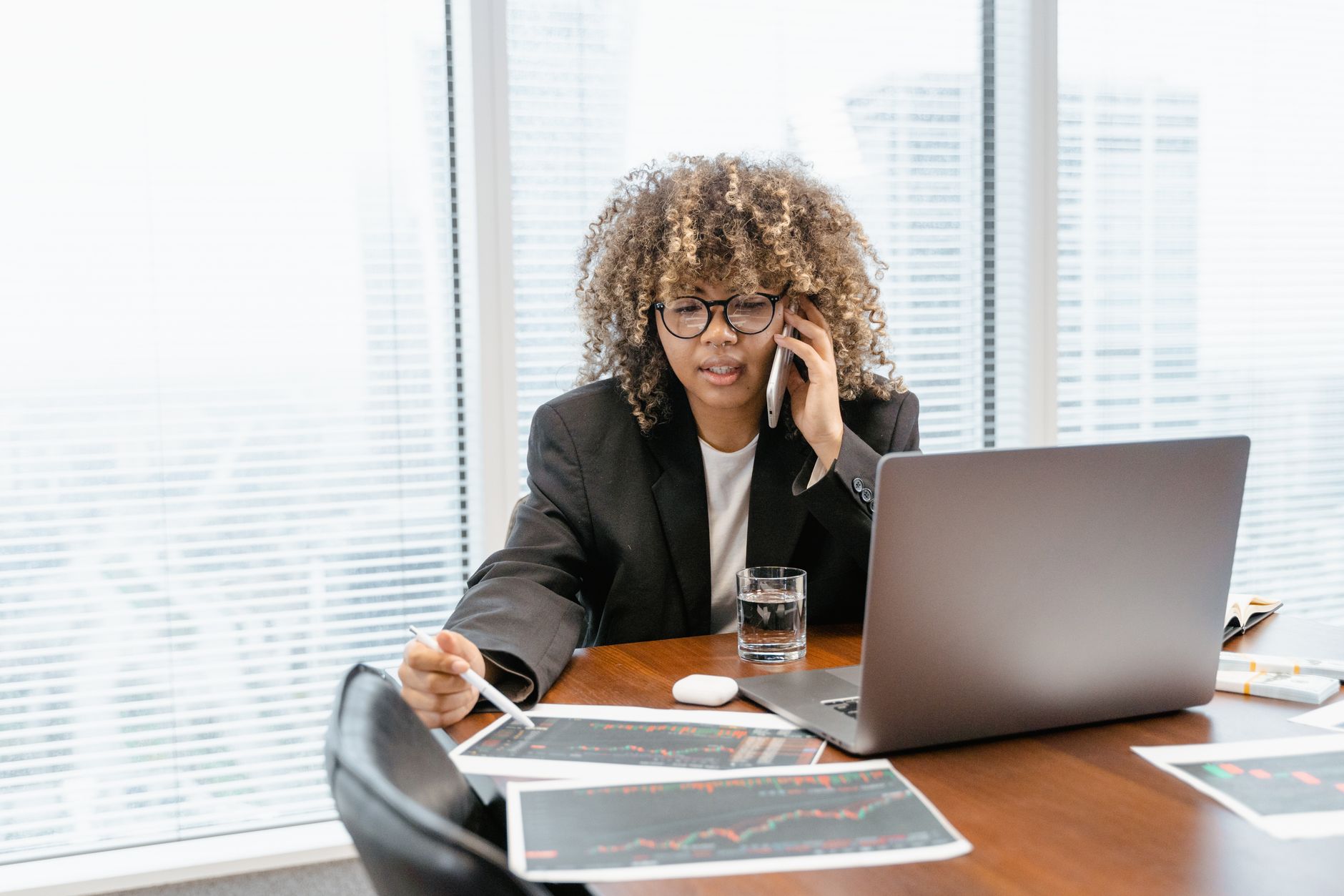 Professional woman multitasking with laptop and phone in modern office setting.