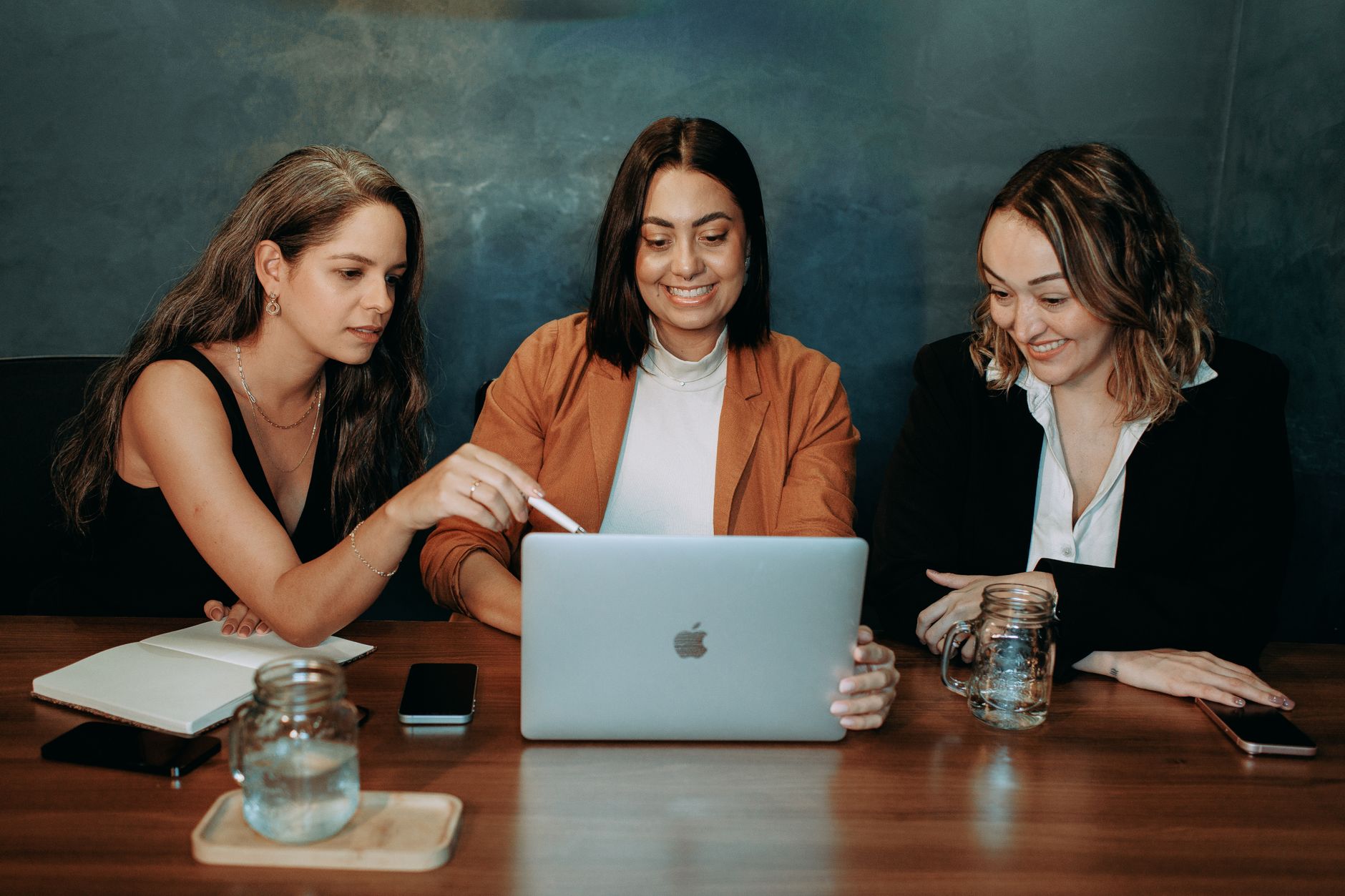 Three women engaged in a business meeting, collaborating on a laptop in a modern office setting.