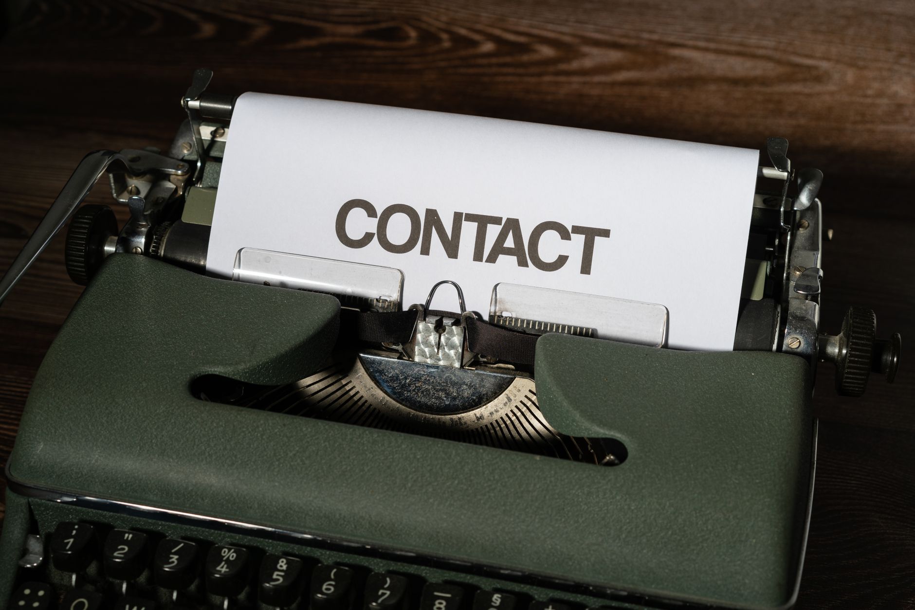 Close-up of a vintage typewriter with a white paper sheet displaying the word 'CONTACT' in bold text.