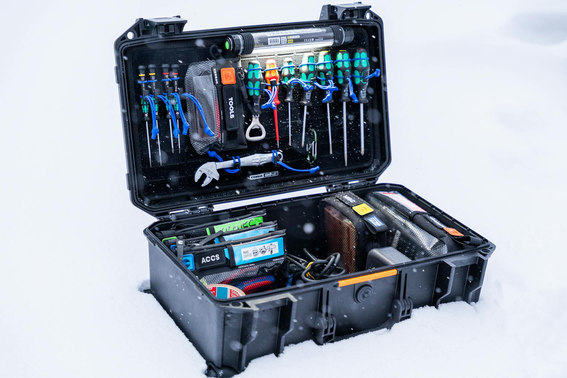 An open professional tool case filled with various tools and equipment, set in a snowy outdoor environment.