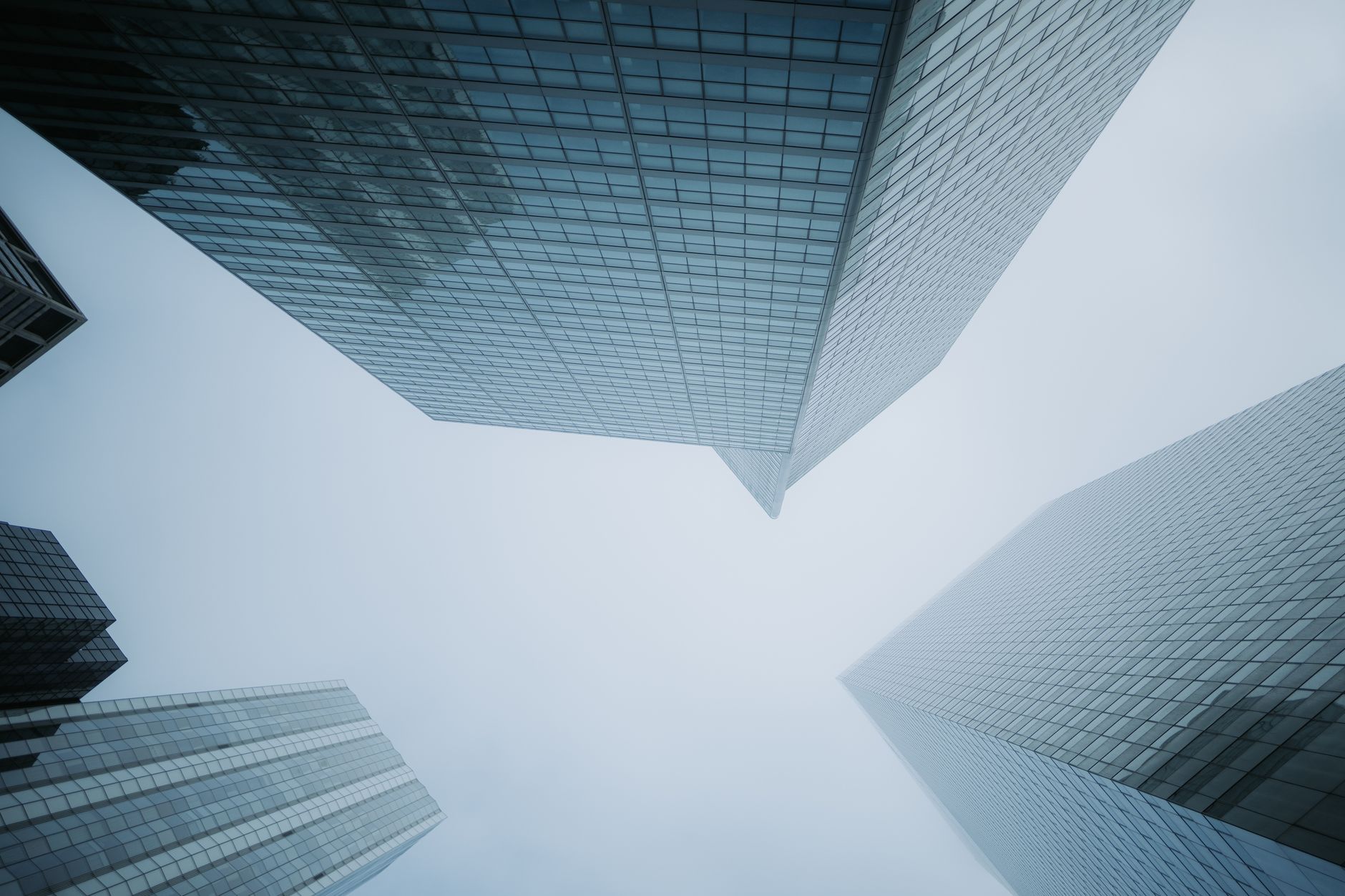Low angle view of modern glass skyscrapers disappearing into the foggy sky, creating a dramatic urban scene.