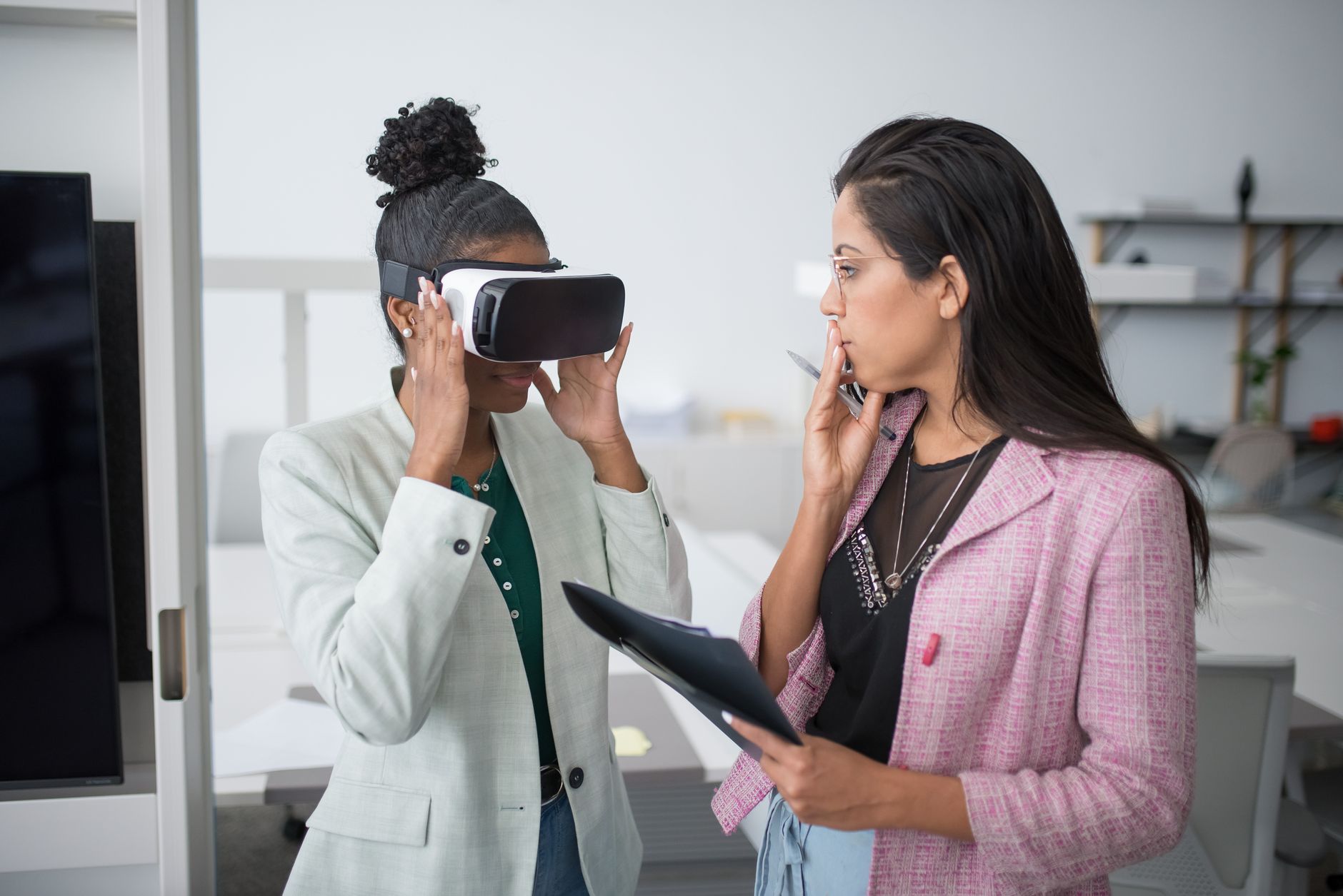Two professional women collaborating using VR technology in a modern office setting, showcasing innovation.