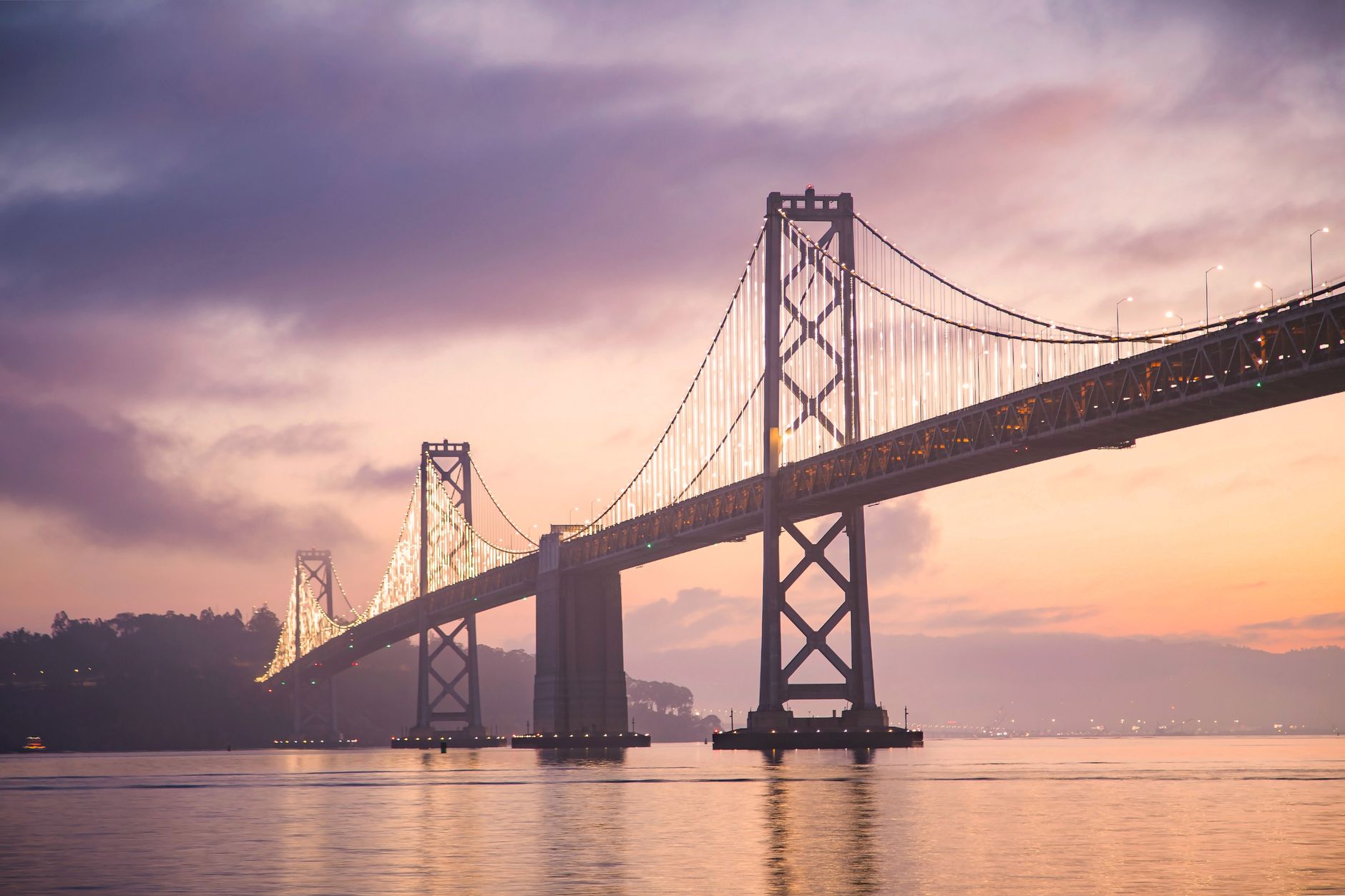 Stunning sunset view of the illuminated San Francisco Bay Bridge with serene waters below.