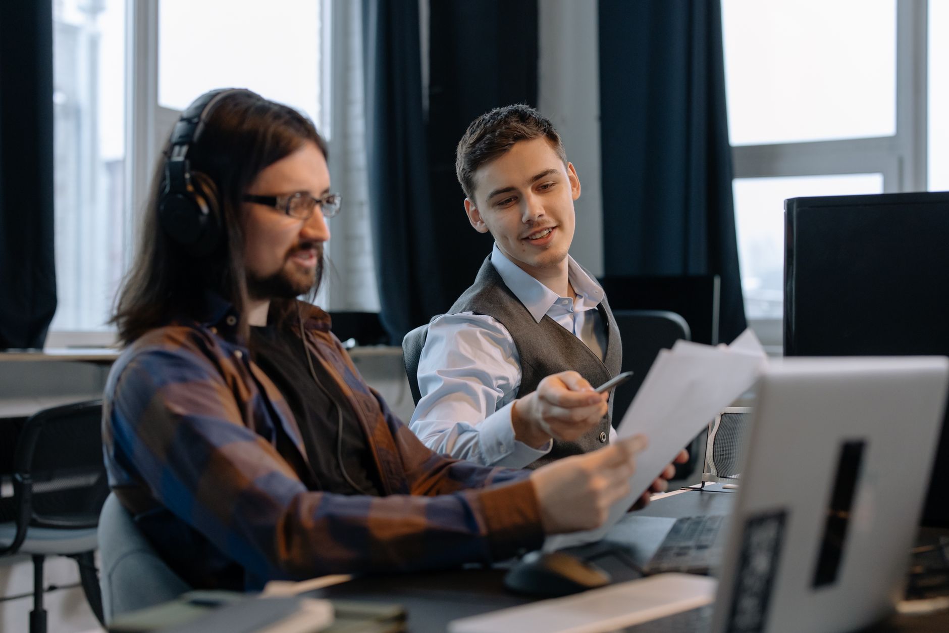 Two colleagues discussing documents at a modern office with computers.