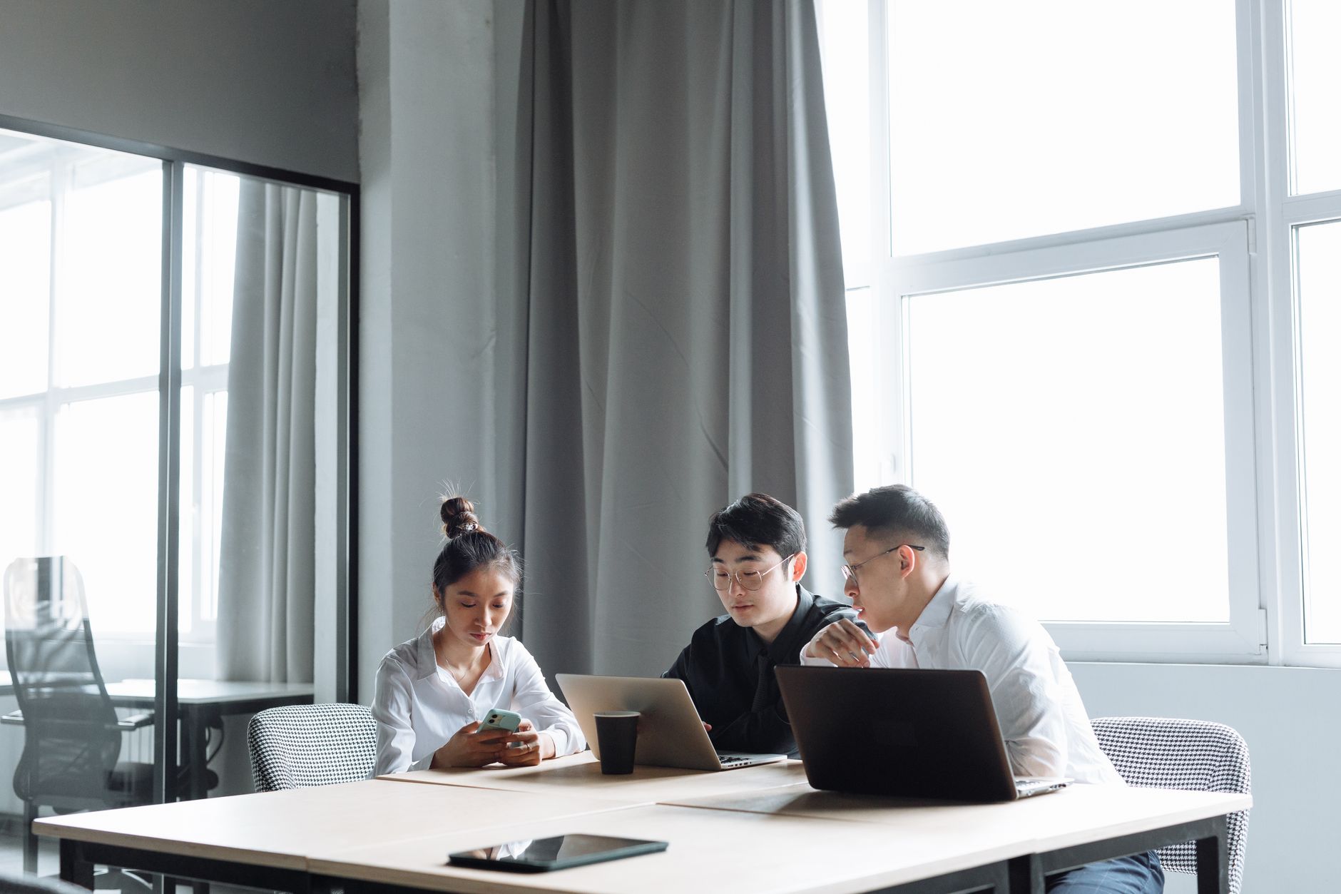 Three professionals collaborate on laptops in a bright, modern office setting.