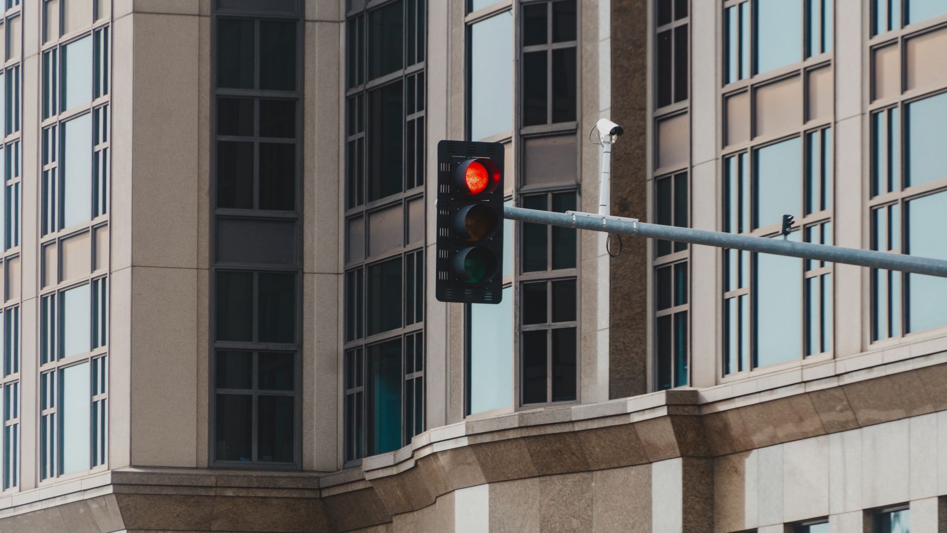 Red traffic light in cityscape setting with modern glass building facade.