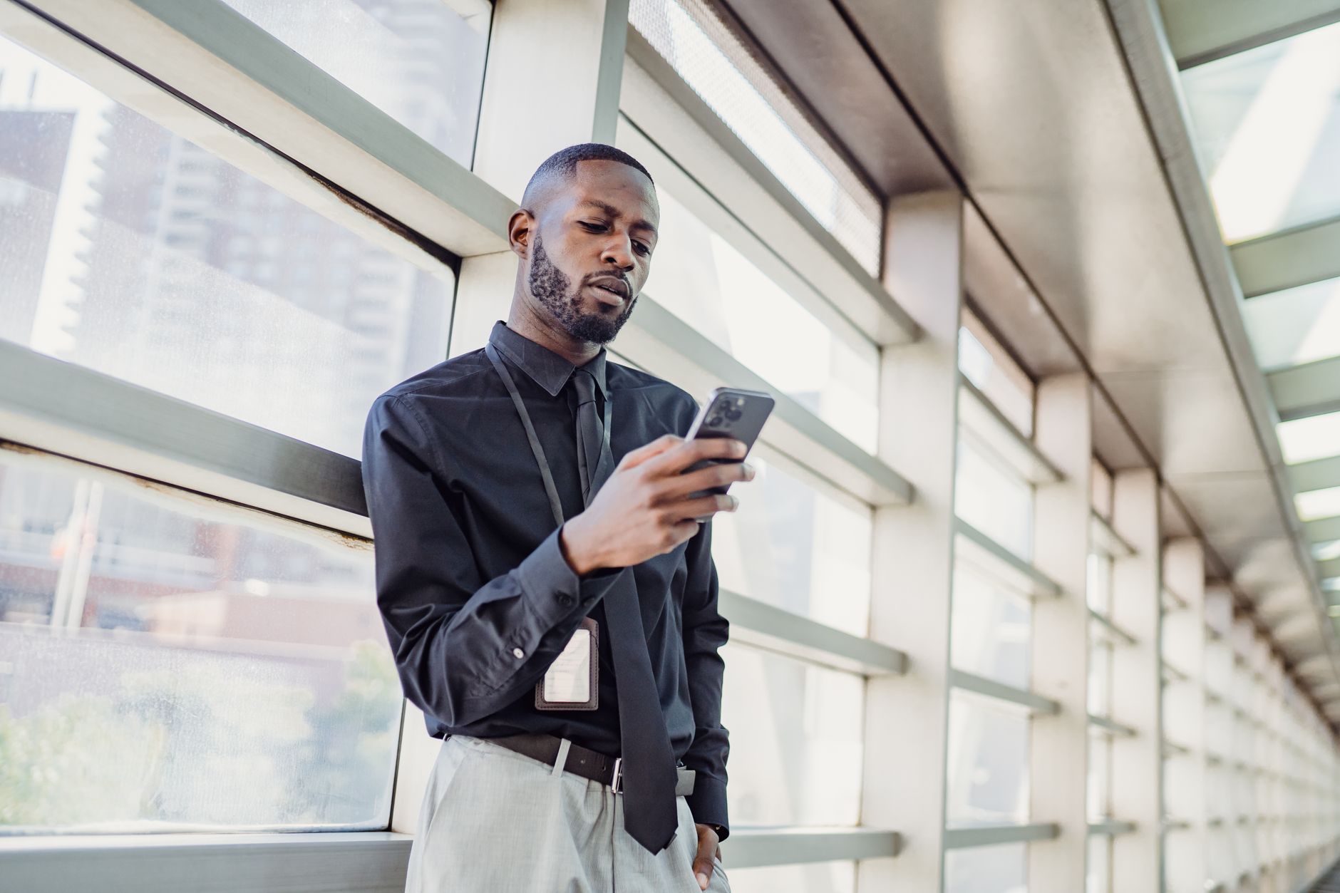Businessman standing indoors using smartphone, modern glass interior.