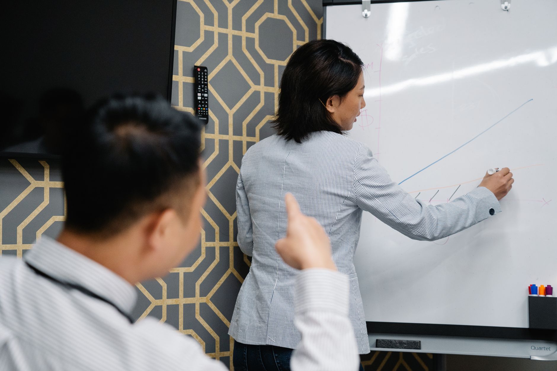 Two professionals in an office discussing a graph on a whiteboard during a business presentation.