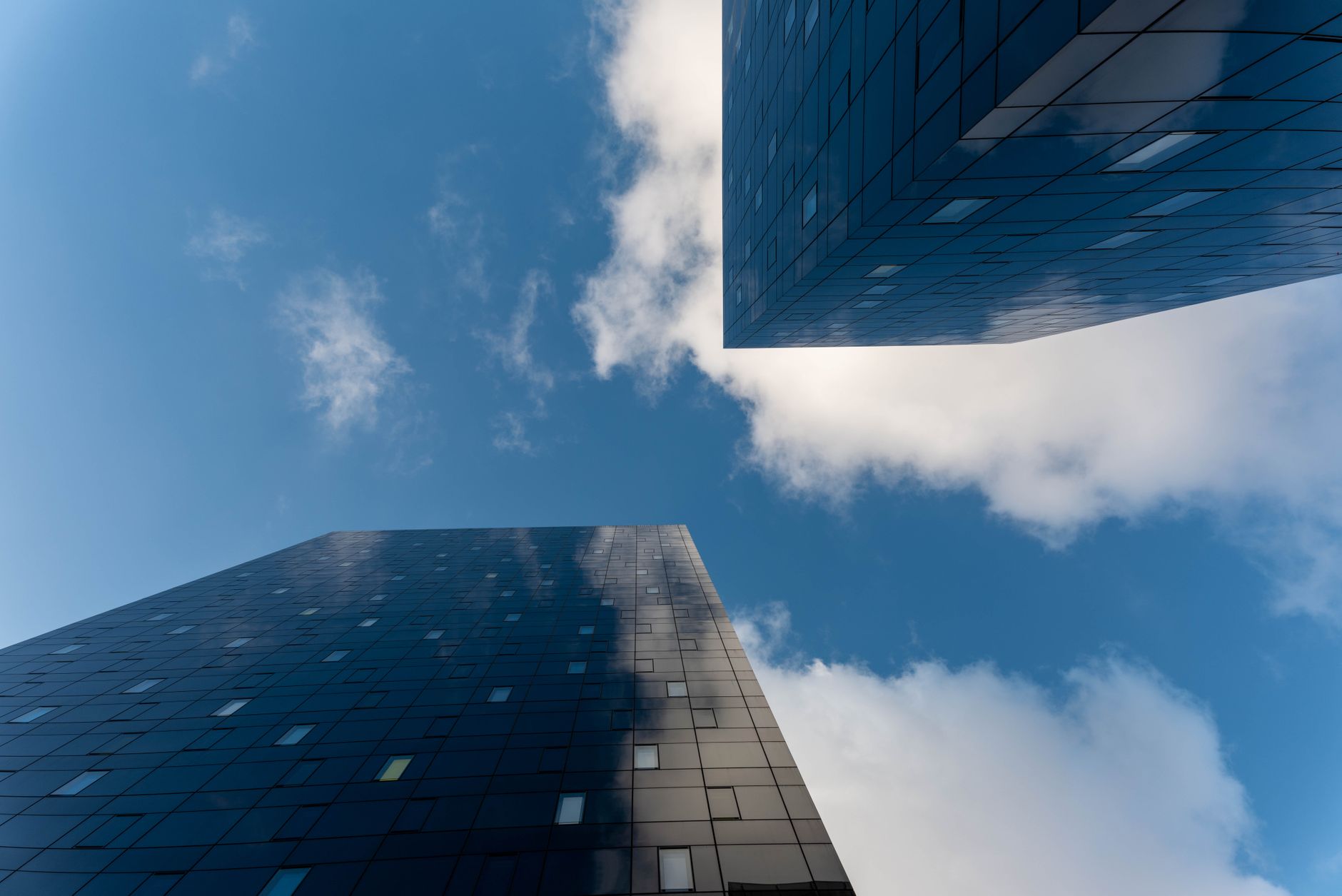 Low angle view of modern glass skyscrapers reaching into a blue sky with scattered clouds.
