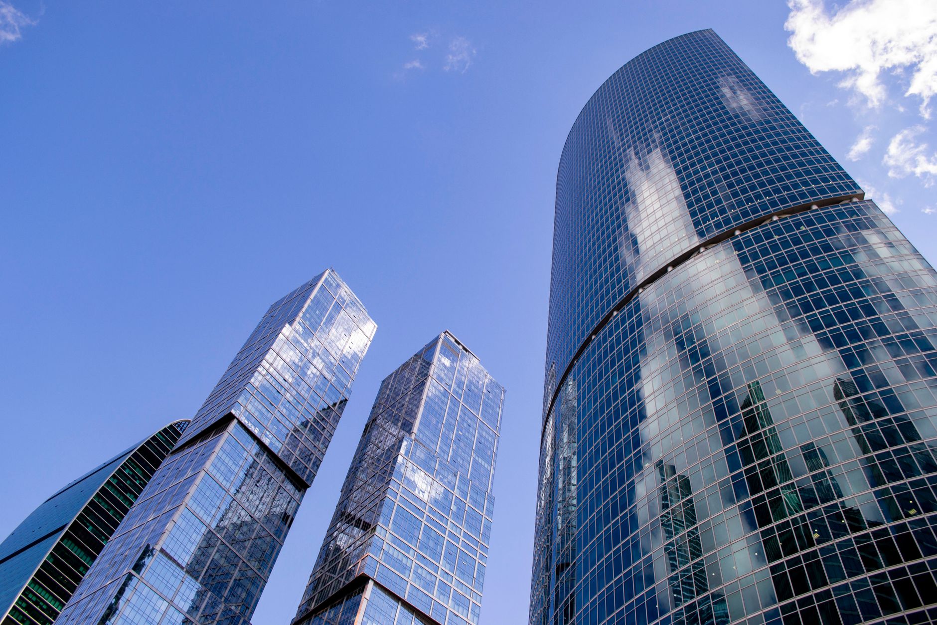 Modern skyscrapers in Moscow with blue glass exteriors and cloud reflections under a clear sky.