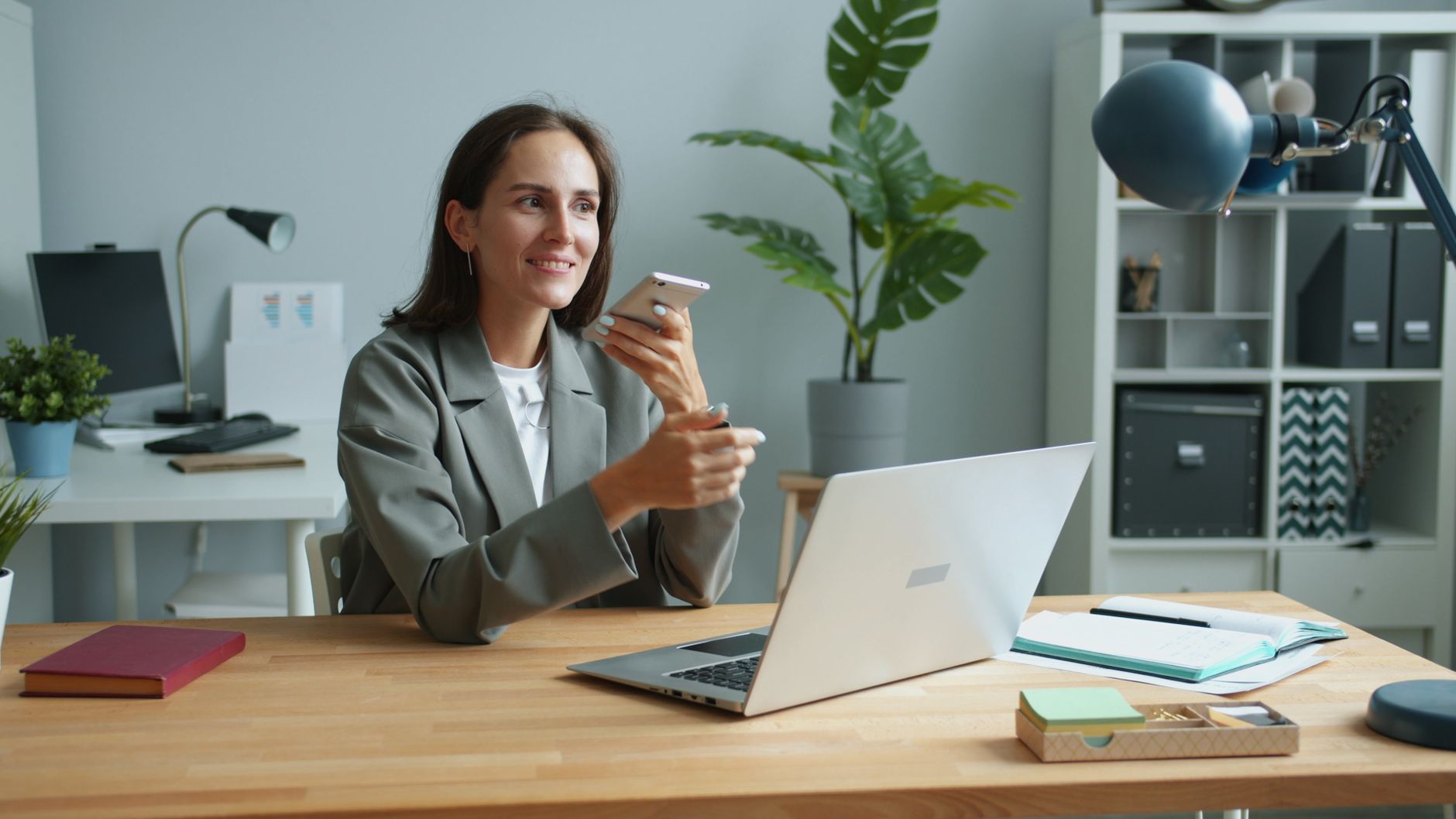 Confident businesswoman using smartphone and laptop in modern office setting.
