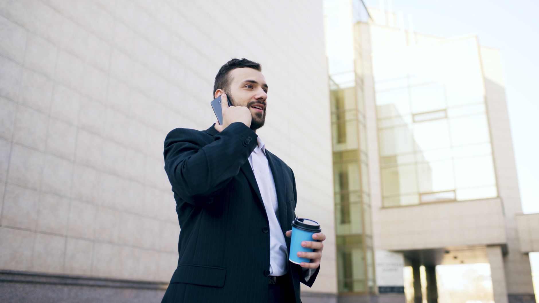 Confident businessman in a suit talking on a phone with a coffee cup in hand.