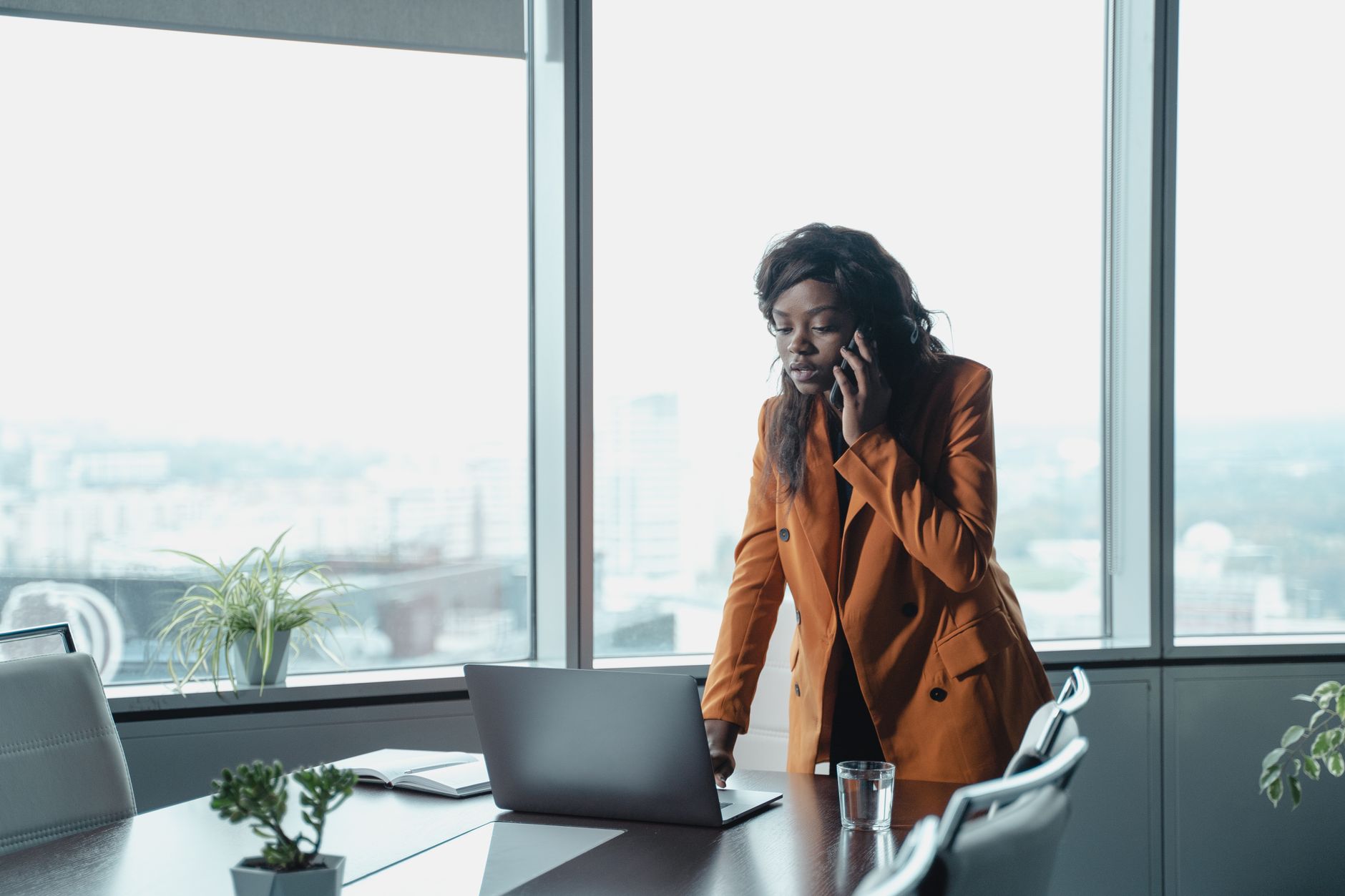 Professional woman in an office setting talking on the phone and working on a laptop.