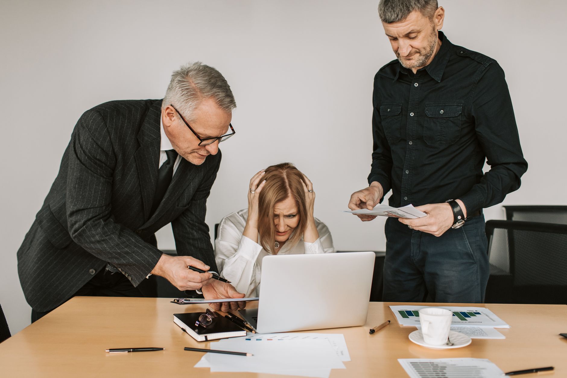 Three business professionals, including an elderly person, in a tense meeting around a laptop.