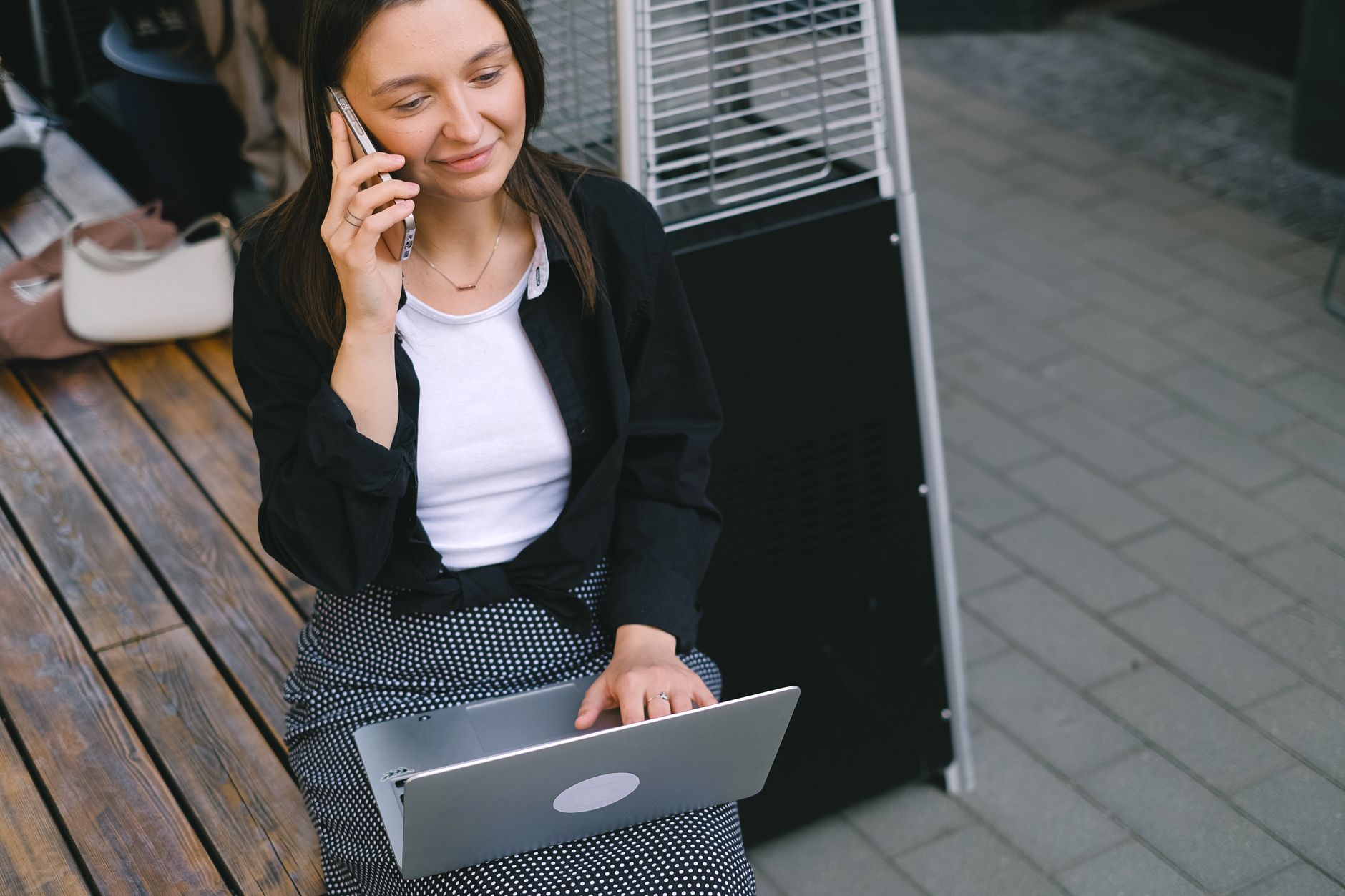 Young woman outdoors sitting with a laptop, talking on the phone. Perfect for business or remote work concepts.