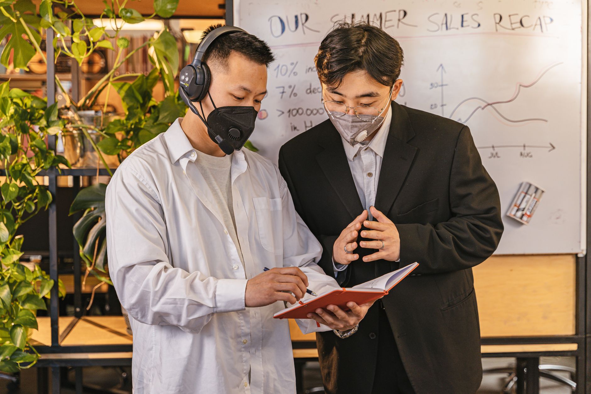 Two professionals in office attire reviewing summer sales data on a whiteboard.