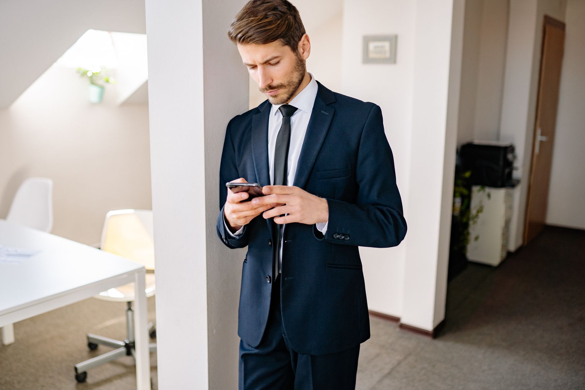 Handsome businessman in a suit checks his smartphone in a modern office setting. Perfect for business themes.