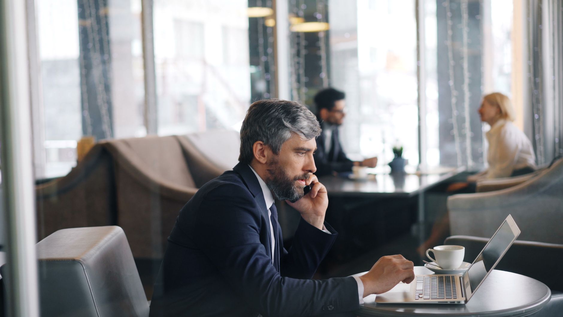 Professional man working on a laptop in a chic café, using a smartphone.