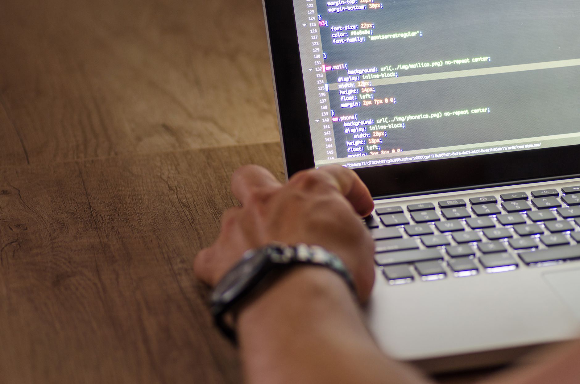 A developer's hand interacting with code on a laptop screen in a workspace setting.