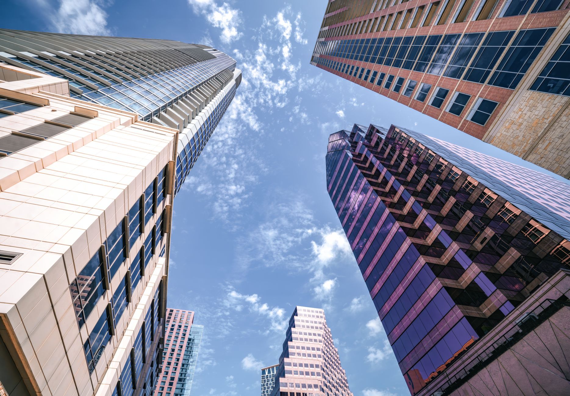 Tall skyscrapers with modern architecture viewed from below against a blue sky.