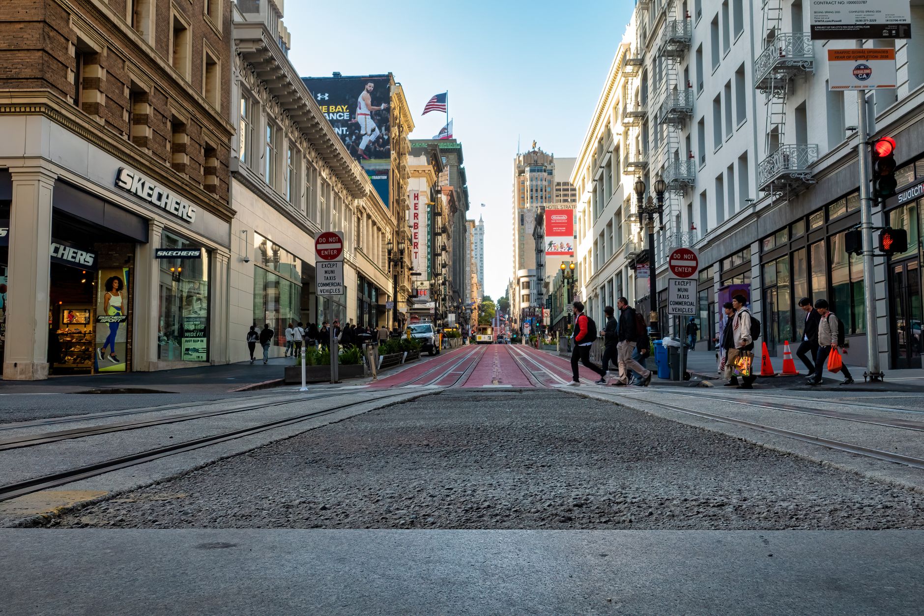 A lively street in San Francisco with people crossing near iconic buildings and shops.