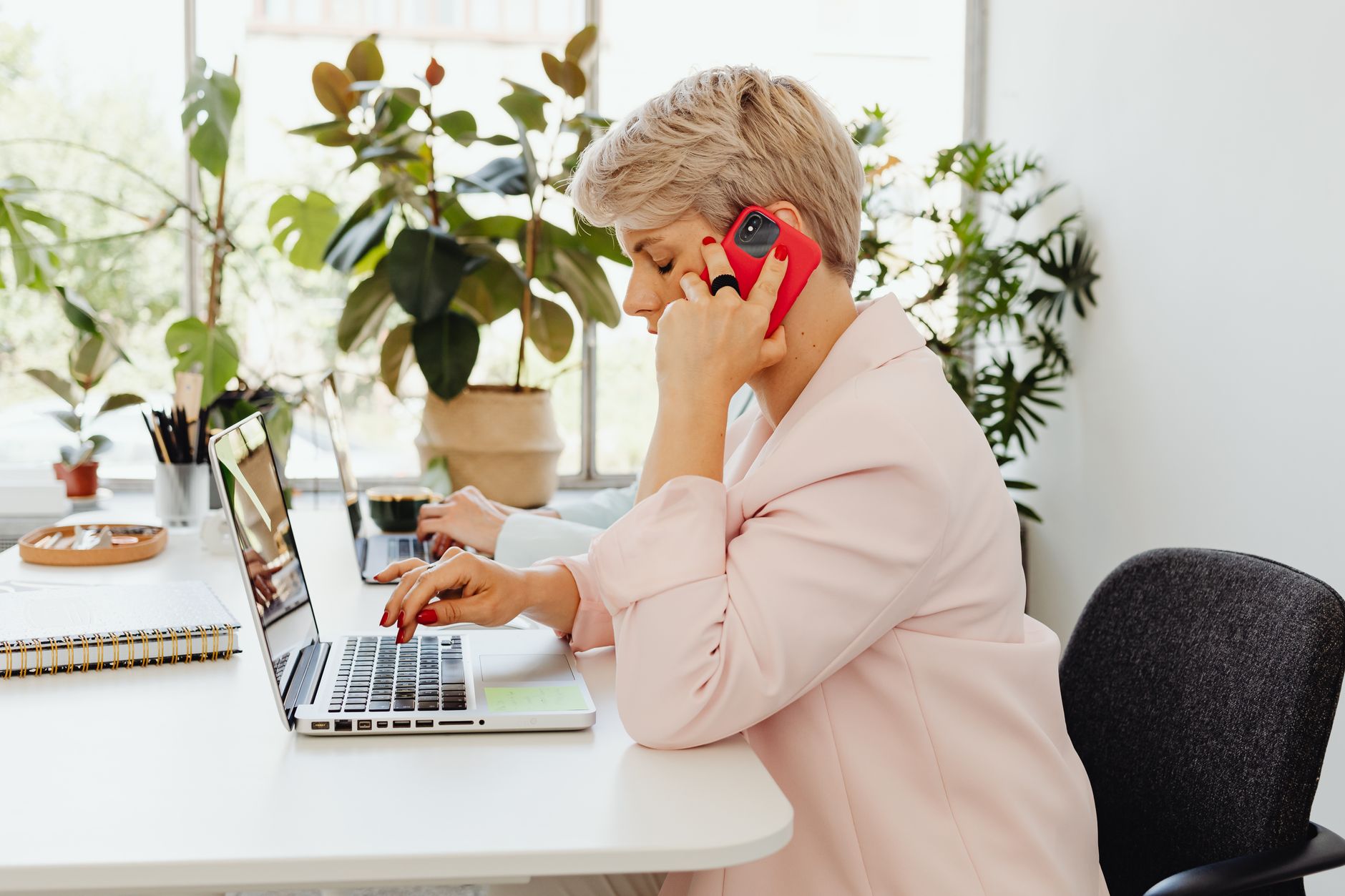 Businesswoman multitasking with a laptop and phone in a modern office environment.