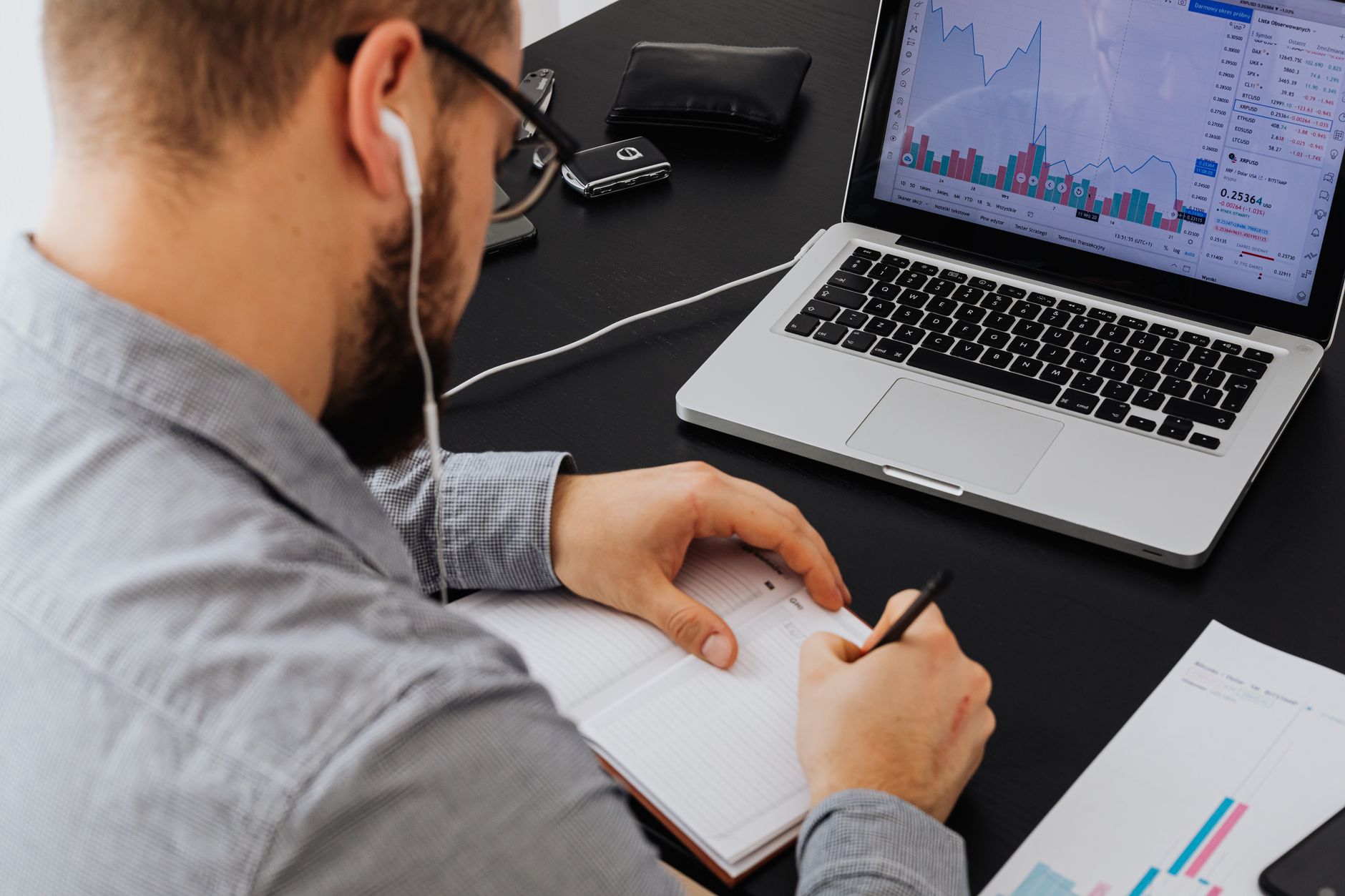 A businessman analyzing stock data on a laptop while taking notes at a desk.