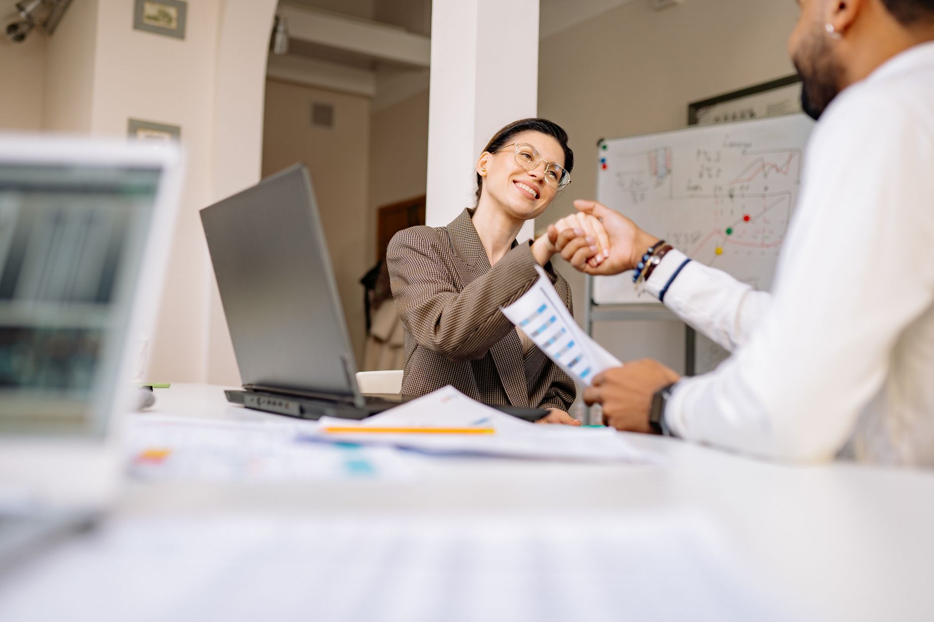 Two professionals smiling and shaking hands in a modern office setting.