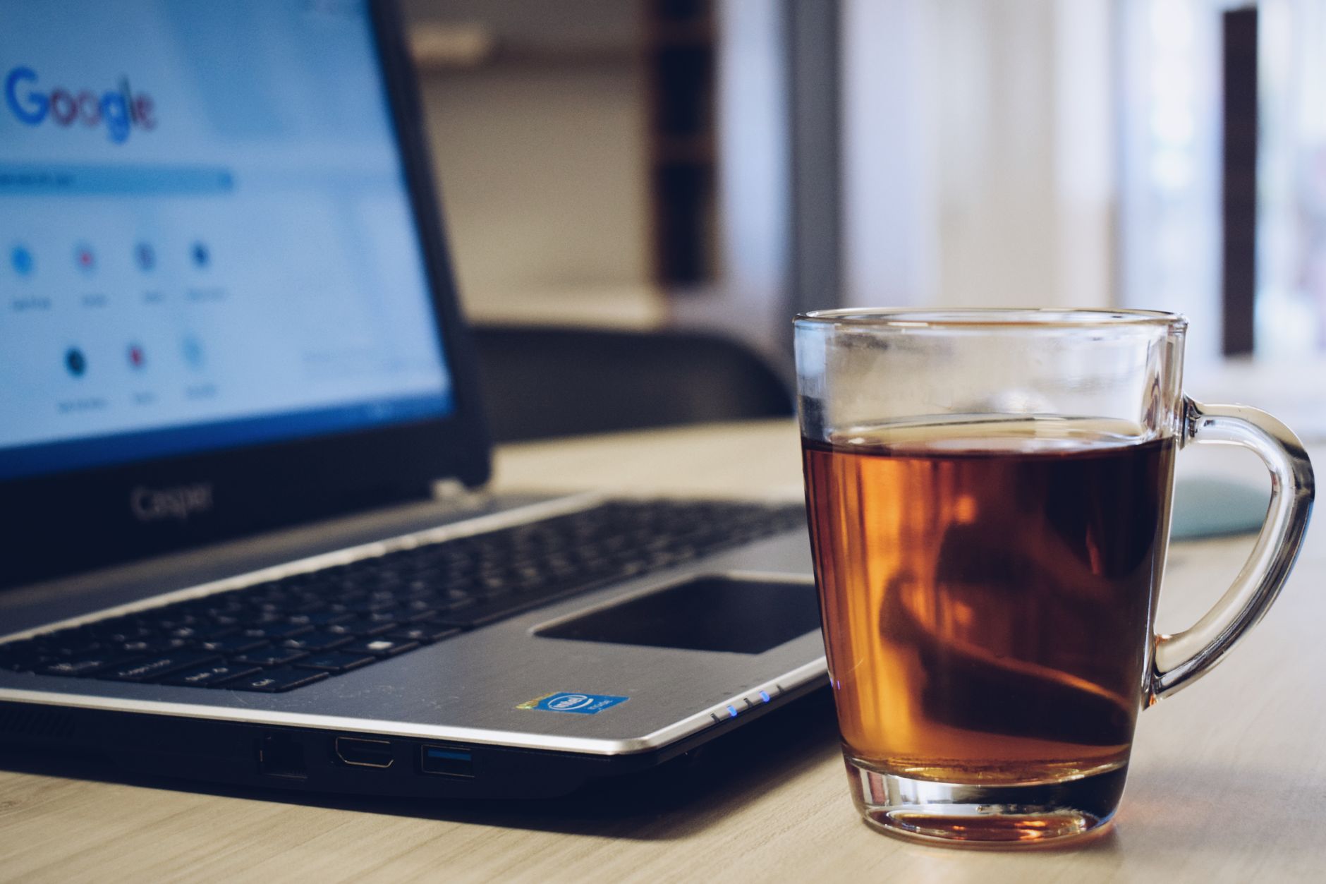 A comforting workspace featuring a laptop and a hot glass of tea on a wooden desk.