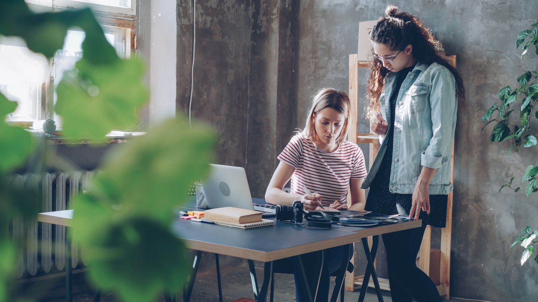 Two women collaborating in a modern office environment surrounded by greenery.